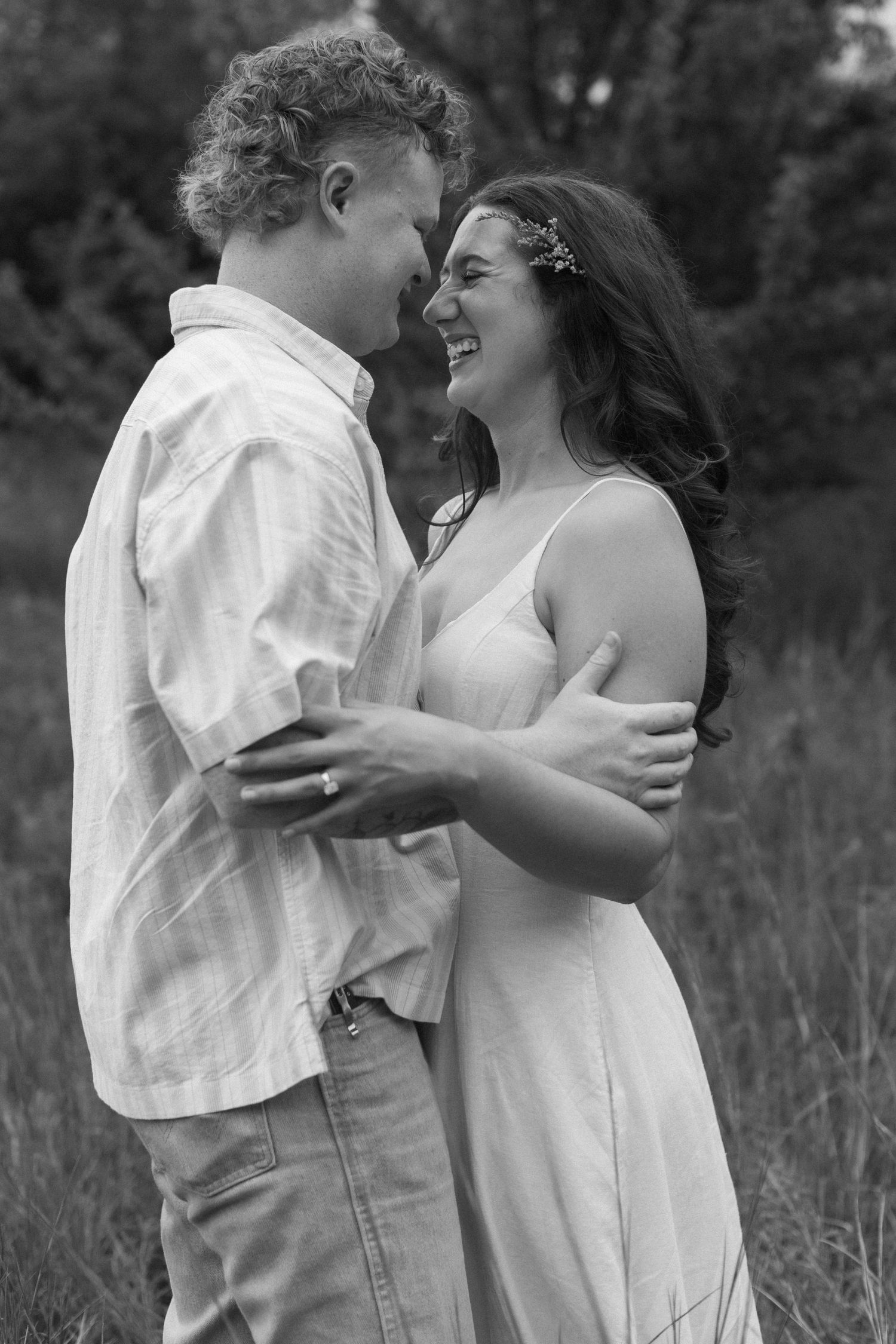 Black and white photo of a couple laughing and embracing in a meadow.