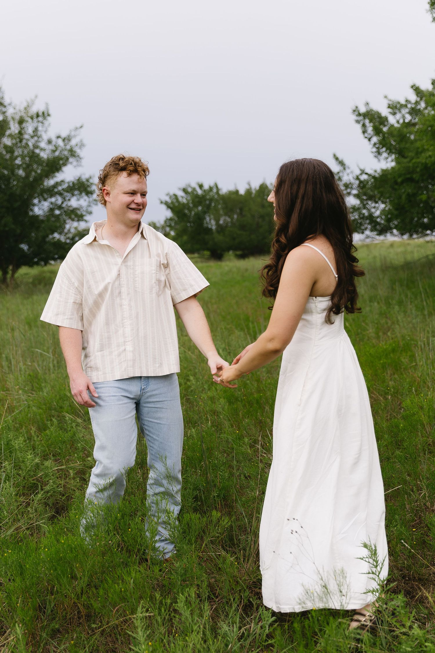 Couple shares joyful moments in white outfits against green meadow backdrop.