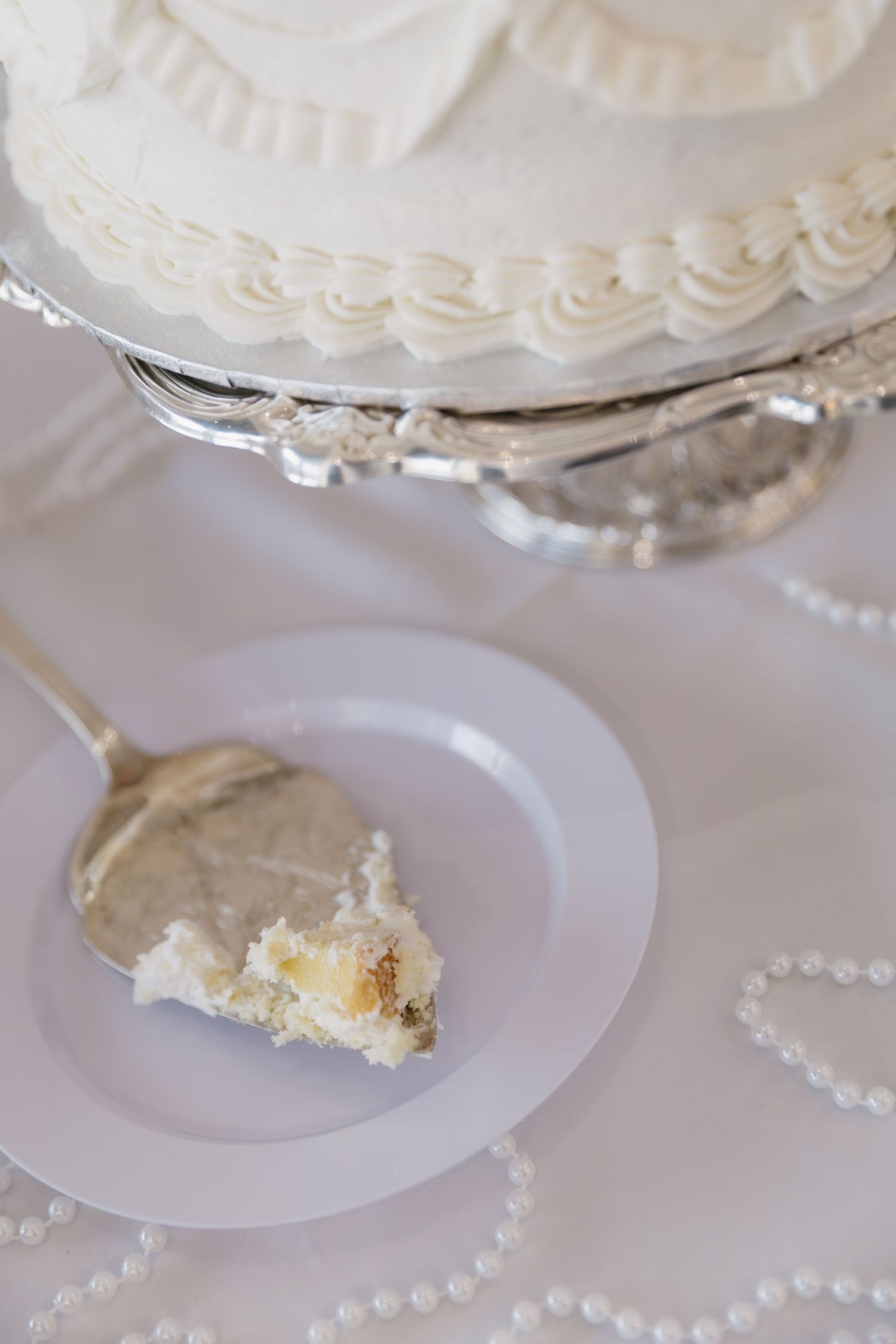 Elegant white wedding cake and pearl decorations on a silver cake stand.