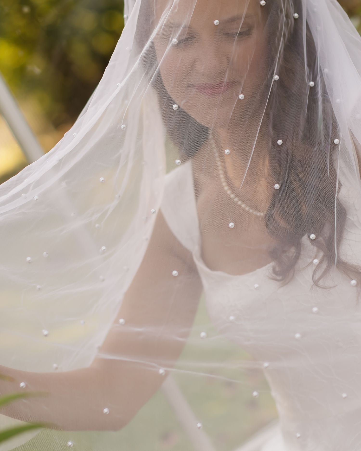 Close-up detail of a delicate pearl-studded bridal veil with soft natural lighting in the background.