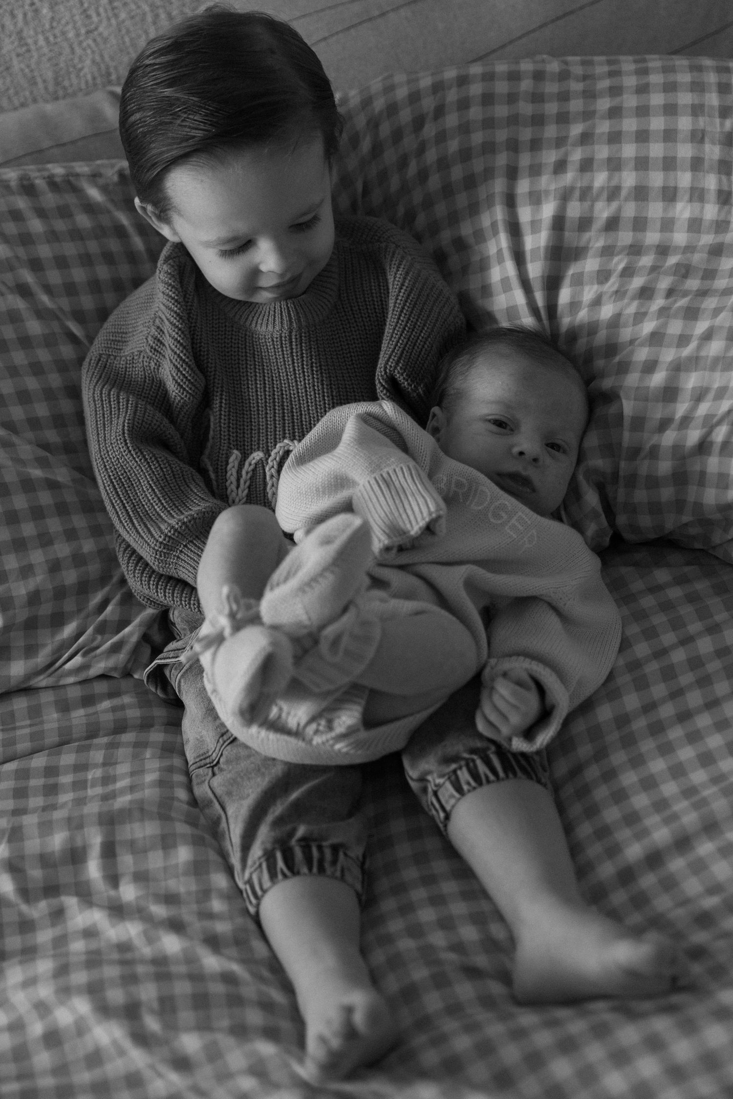 Two children share a quiet moment together on a gray checkered couch.