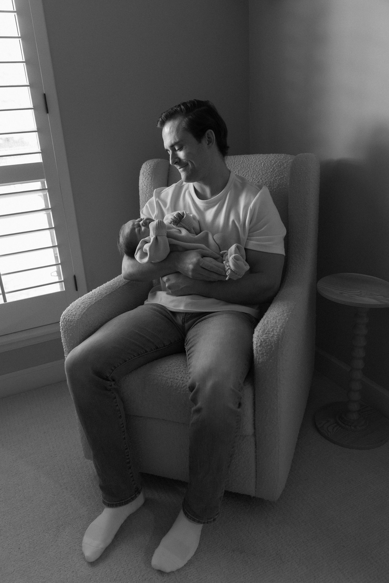 Family relaxing together on gray armchair in naturally lit room.