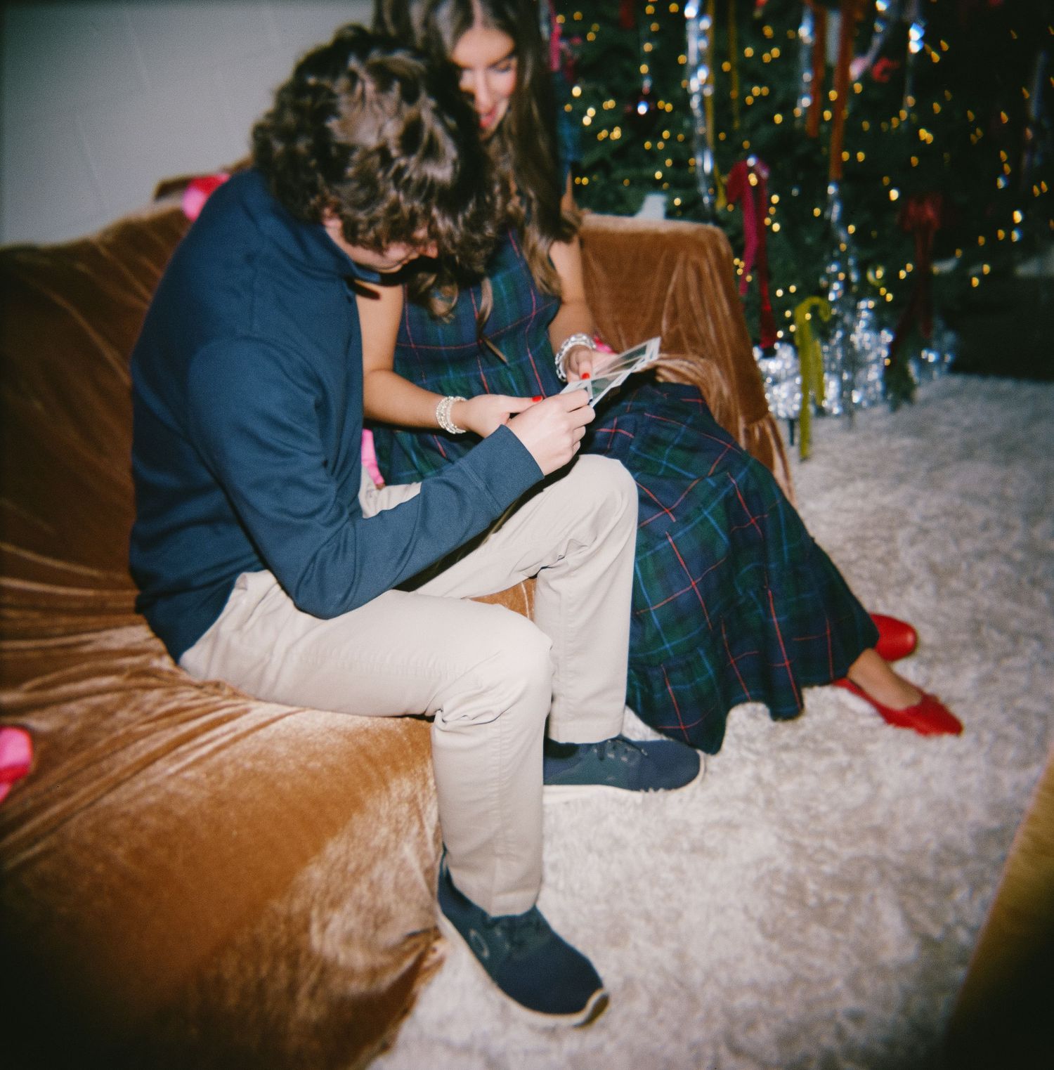 A couple sits together on a beige couch with a decorated Christmas tree glowing in the background.
