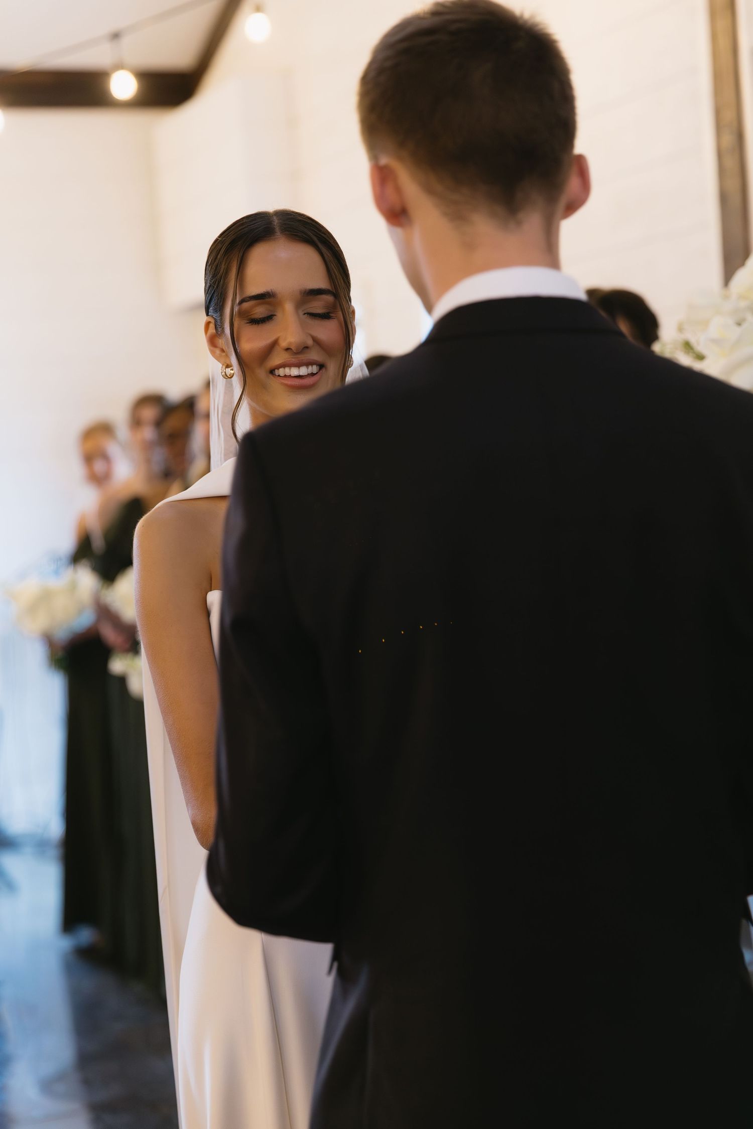 Intimate indoor wedding ceremony moment with bride in white dress and guests watching.