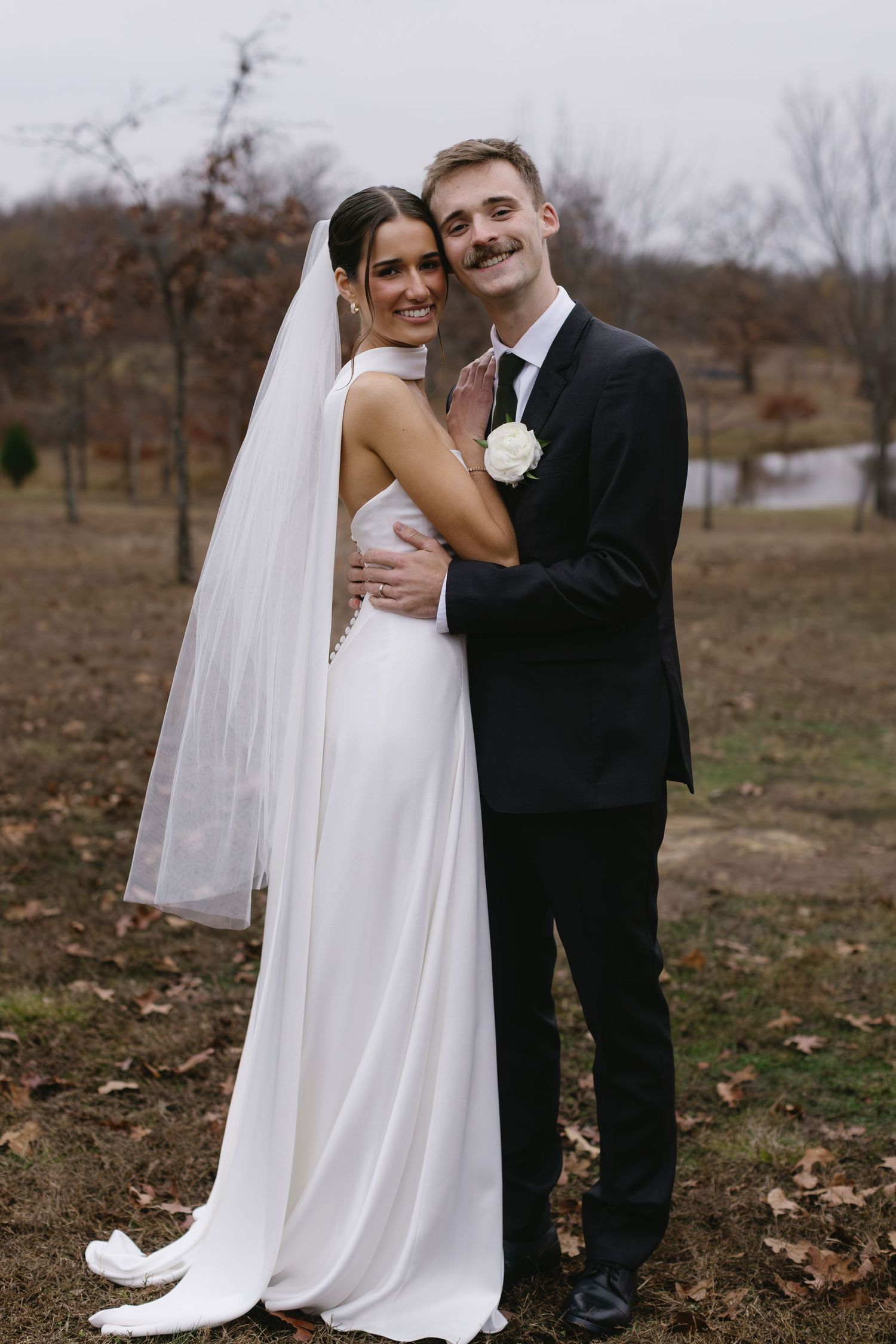 Couple embraces during outdoor wedding photos surrounded by fallen autumn leaves.