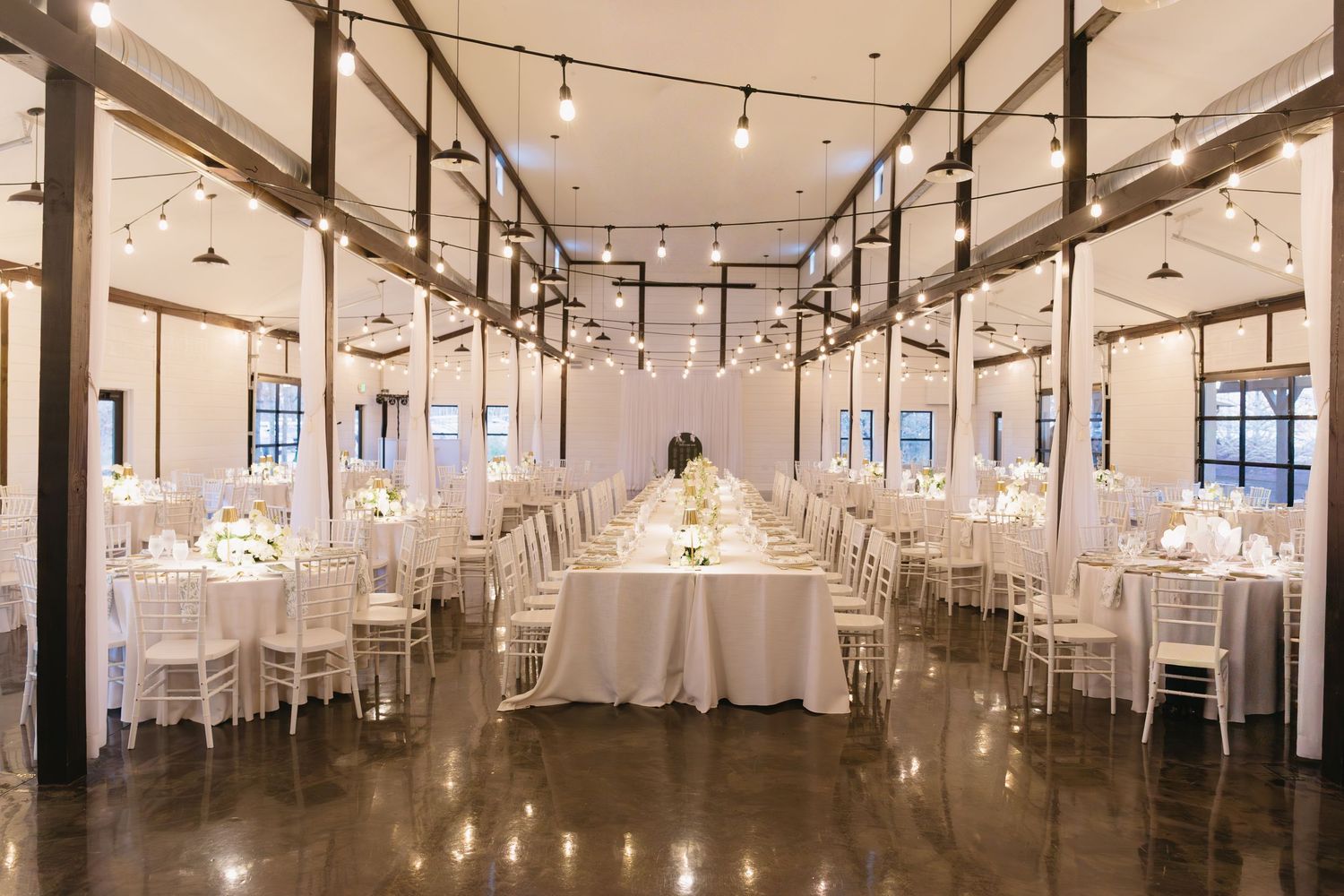 Elegant white wedding reception hall with string lights and high ceilings.