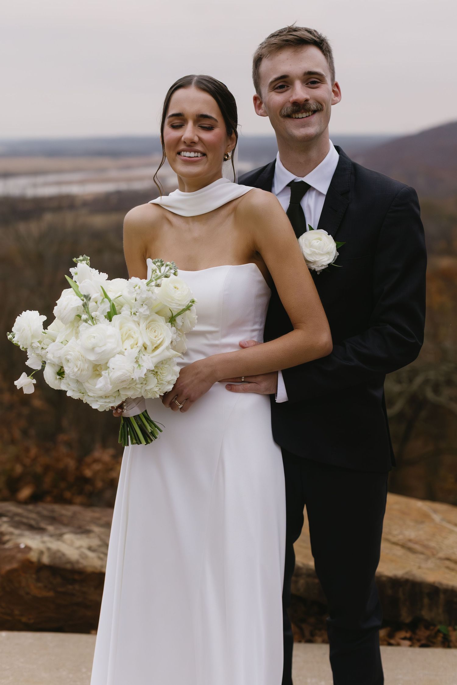 Newlyweds pose together on a mountaintop holding a stunning white floral bouquet.
