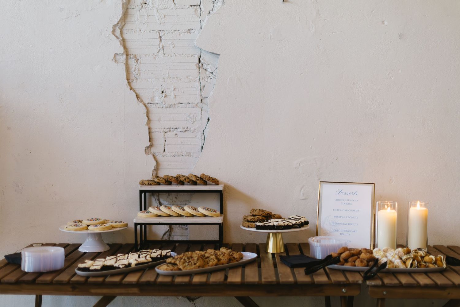 A minimalist dessert display table with candles against a white brick wall.