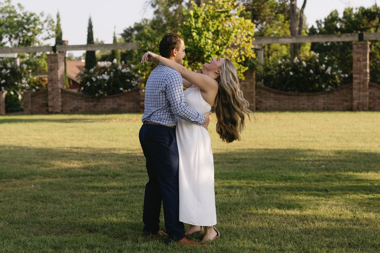 Two figures embrace tenderly during a romantic golden hour photoshoot in a lush garden setting.
