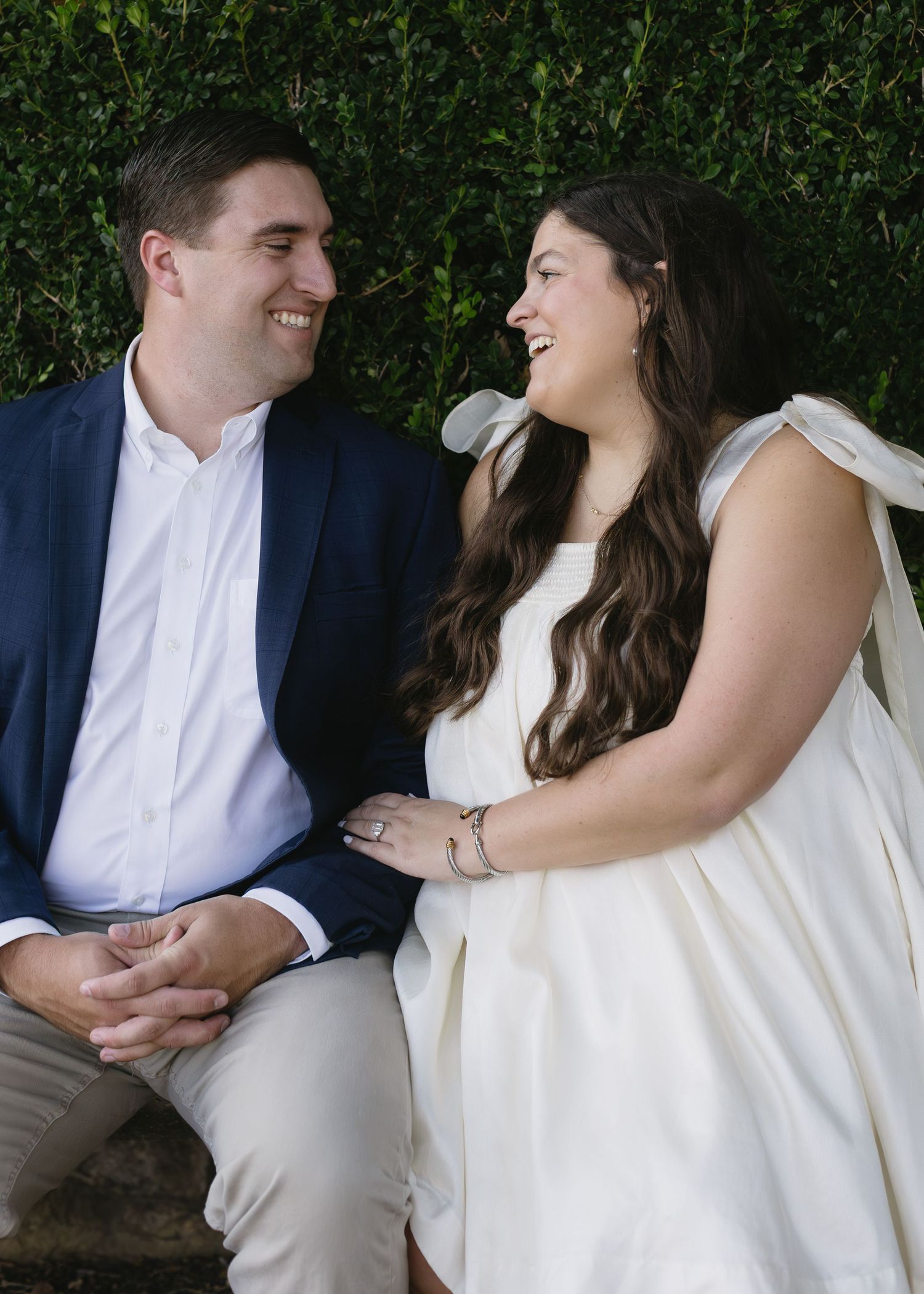 A couple shares intimate moments in formal attire while seated outdoors against a dark green backdrop.
