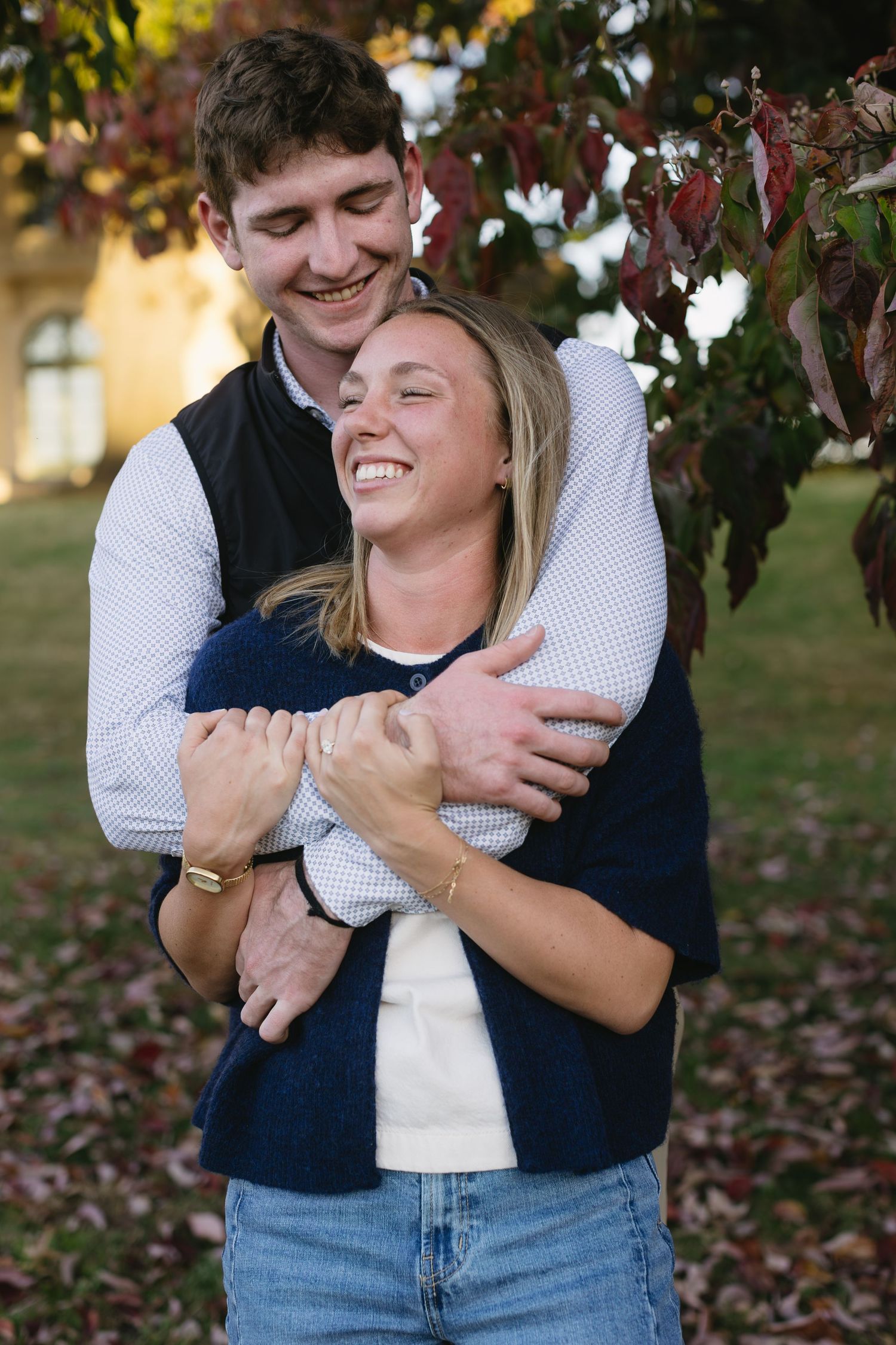 Candid moment of a couple embracing and laughing together outdoors near autumn foliage.