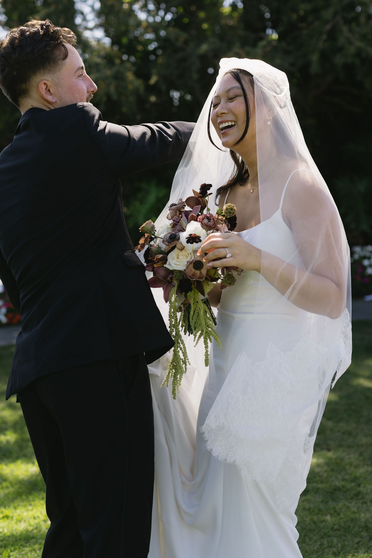 Joyful outdoor wedding scene with newlyweds laughing and embracing in natural sunlight.