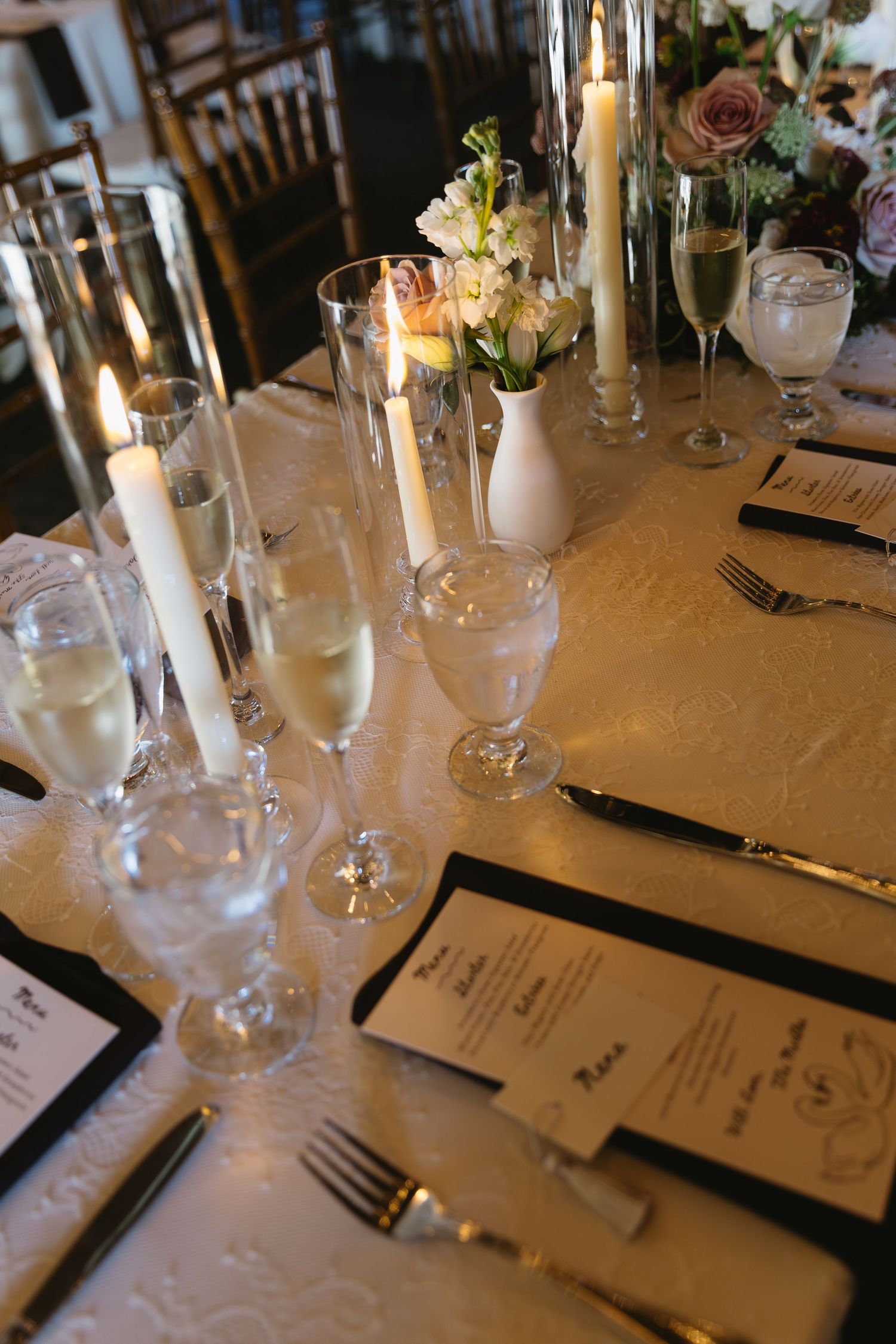 Wedding reception table settings with glowing candles, crystal glasses and printed menus.