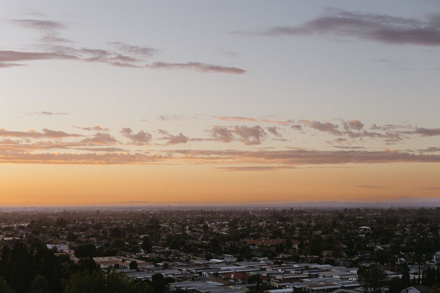 Panoramic sunset view of a city skyline with pink and orange clouds.