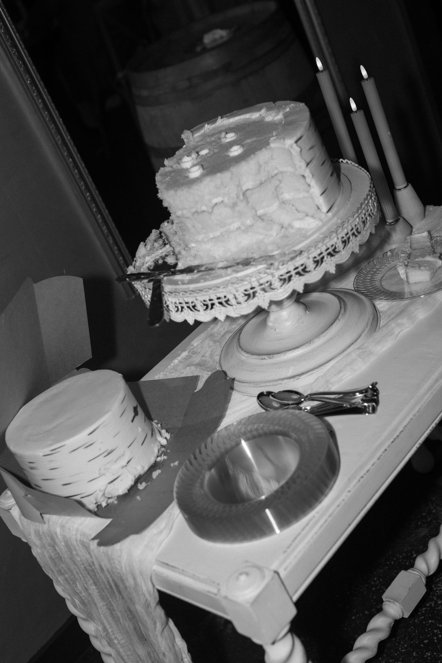 Black and white photo of a wedding cake with candles on an elegant table setting.