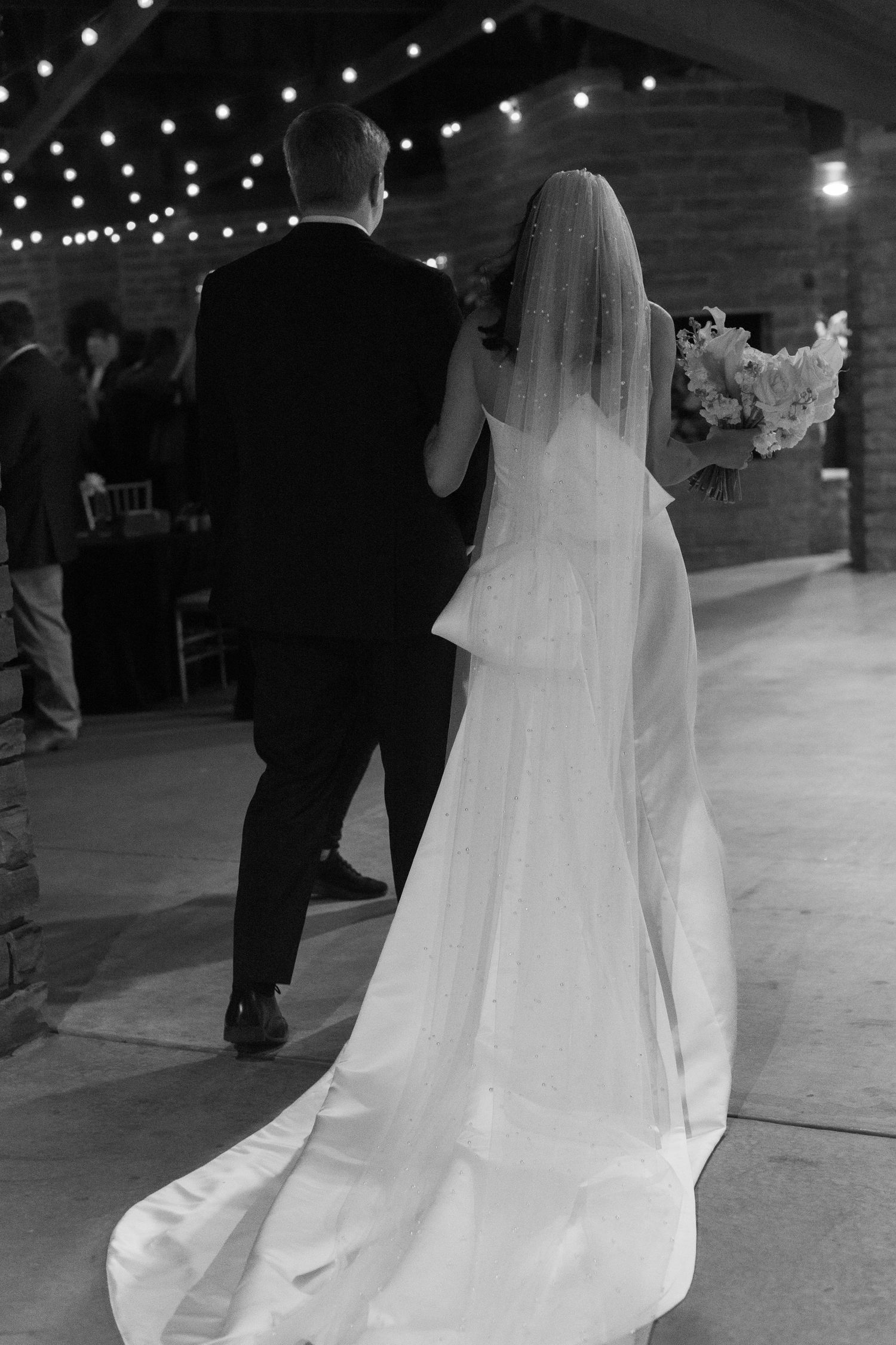 Bride in flowing white dress dances under twinkling lights at wedding reception.