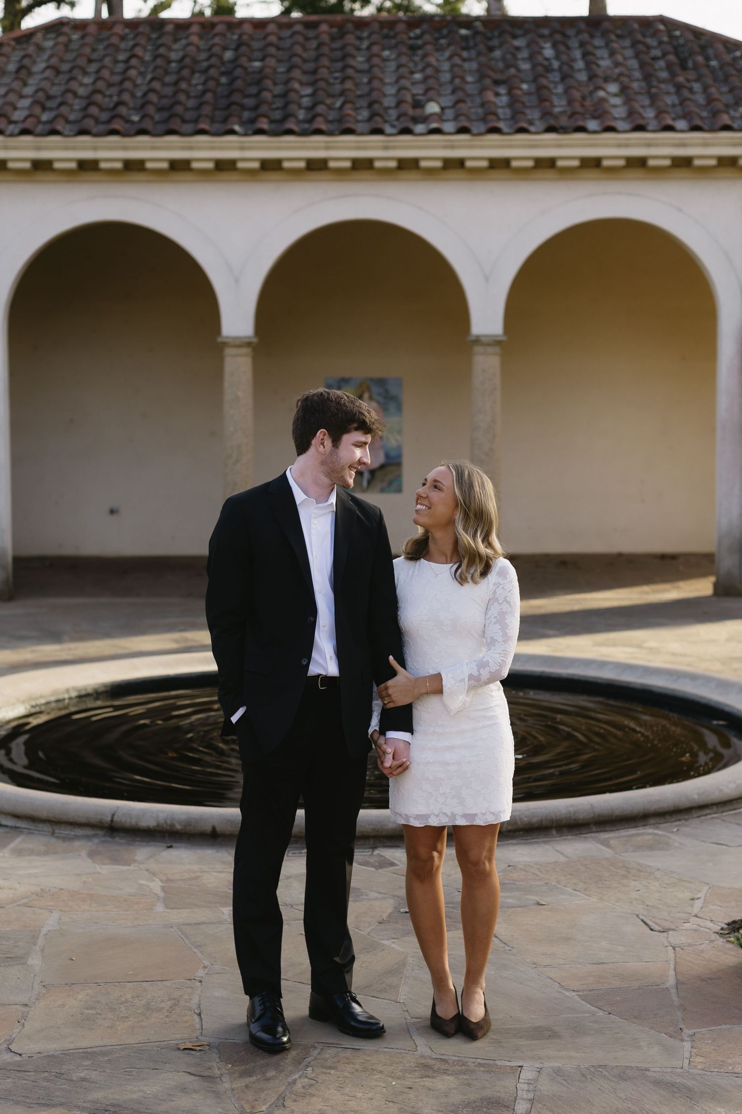 A couple shares an intimate moment near stone columns and arches.