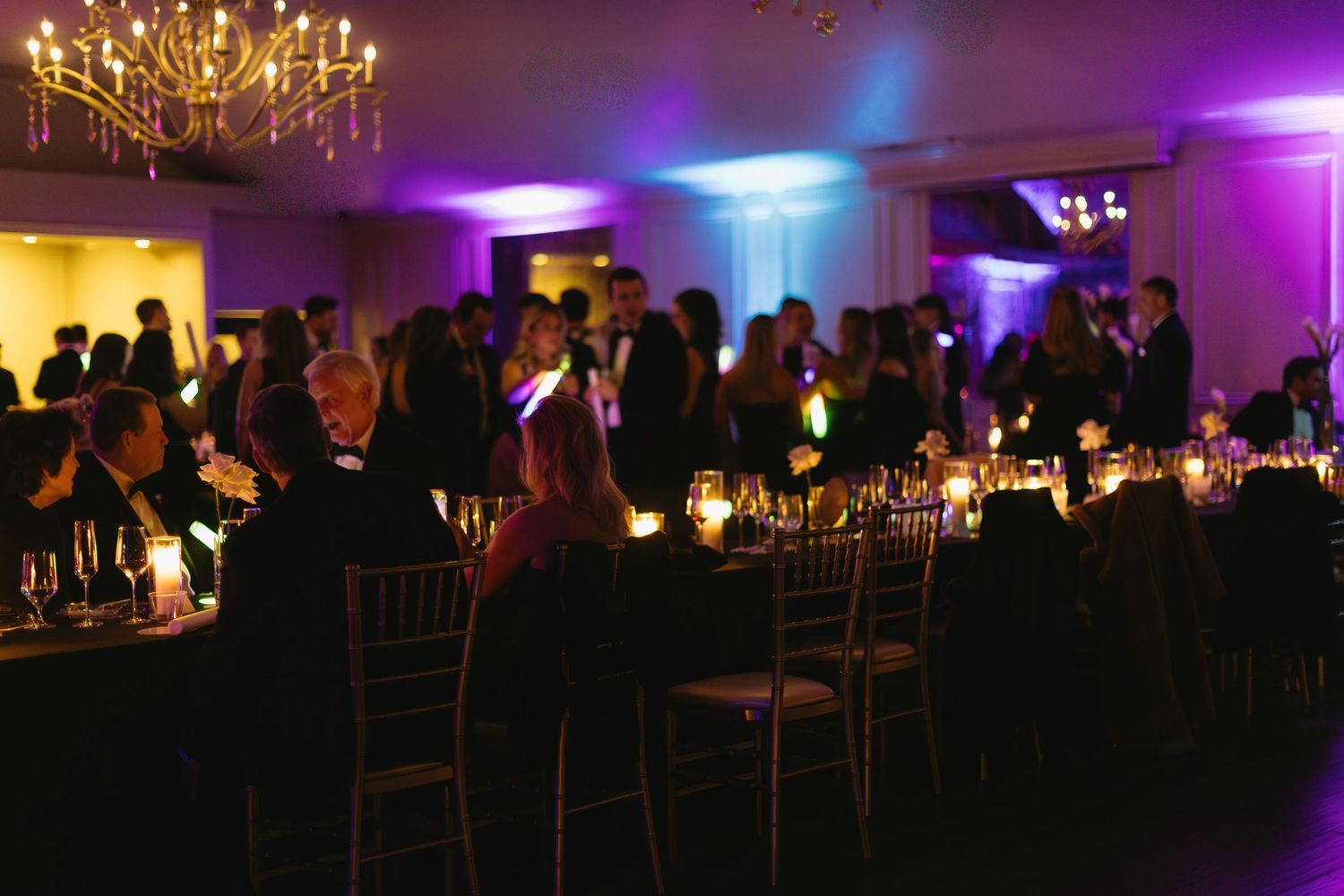 Dimly lit wedding reception with chandelier and purple mood lighting.