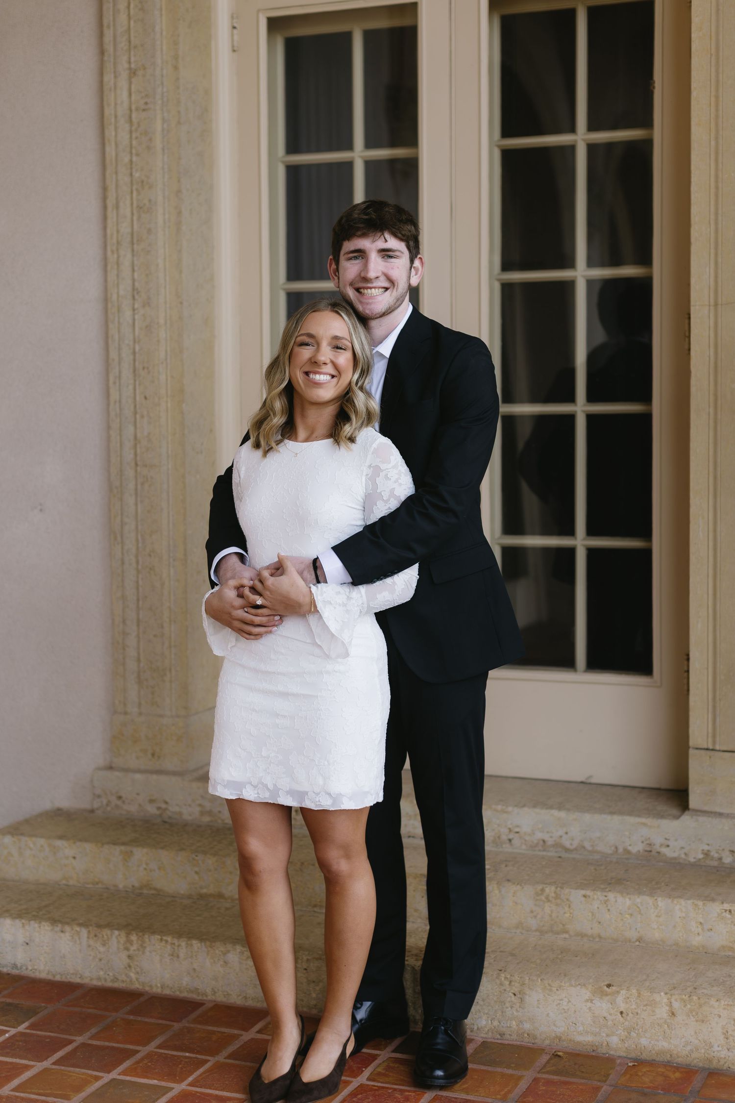 A romantic couple pose together in formal attire against a classic architectural backdrop.