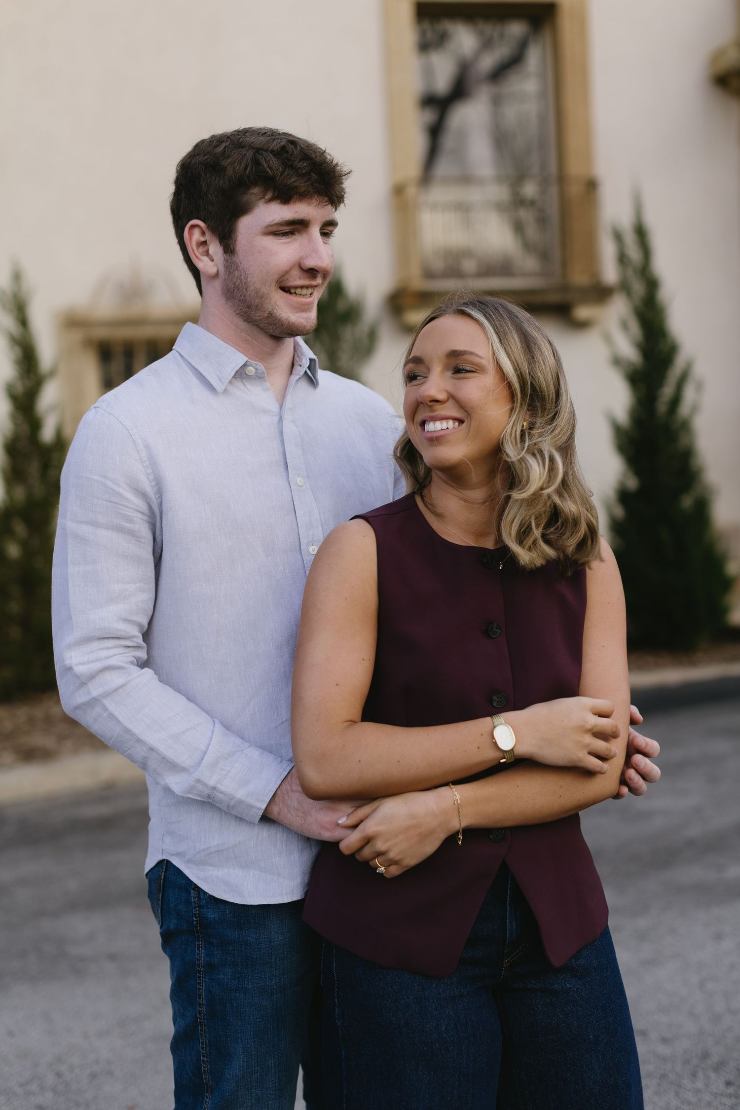 A couple shares joyful laughter during their outdoor engagement photo session in casual attire.
