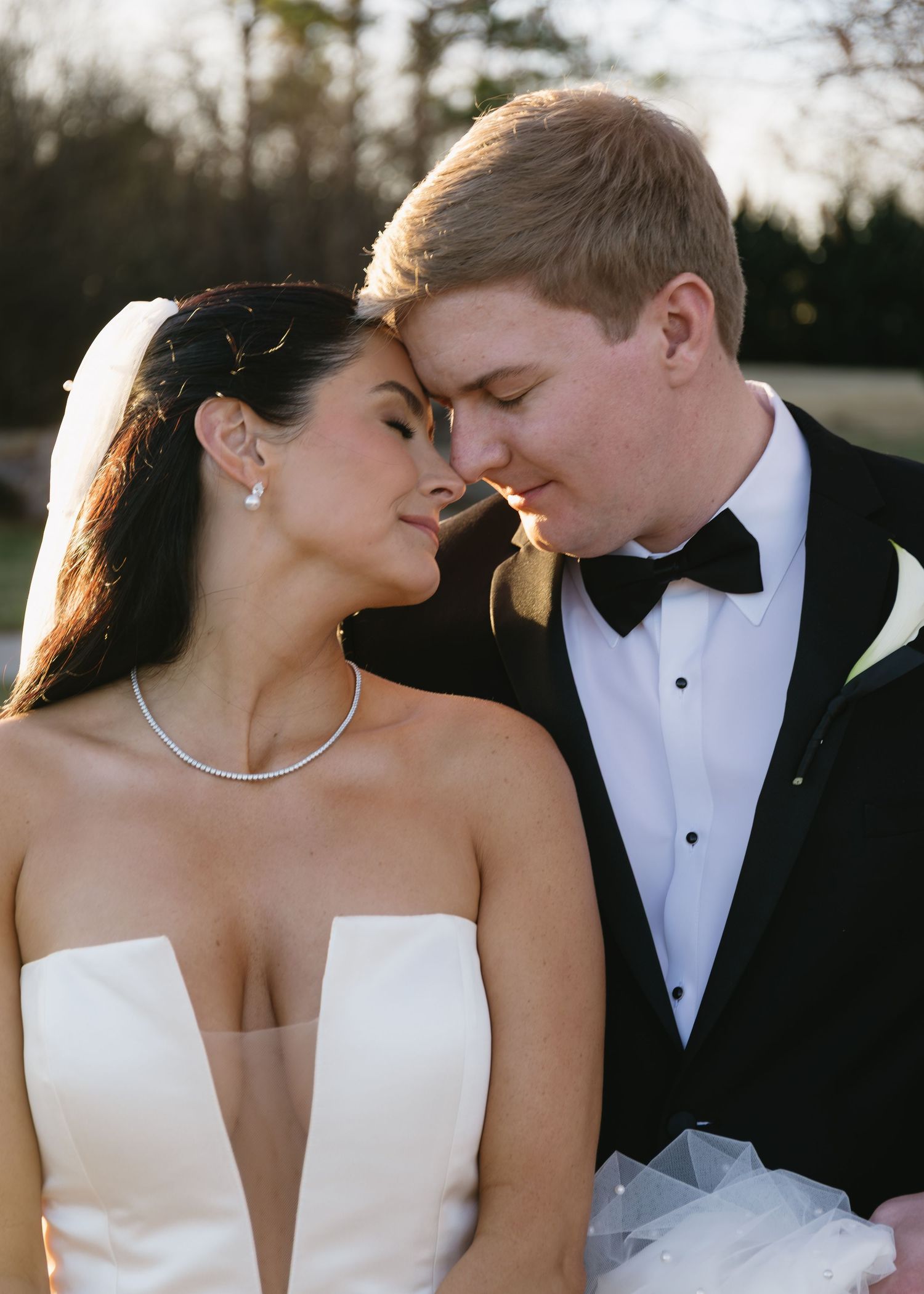 A tender moment between newlyweds in formal attire during golden hour.
