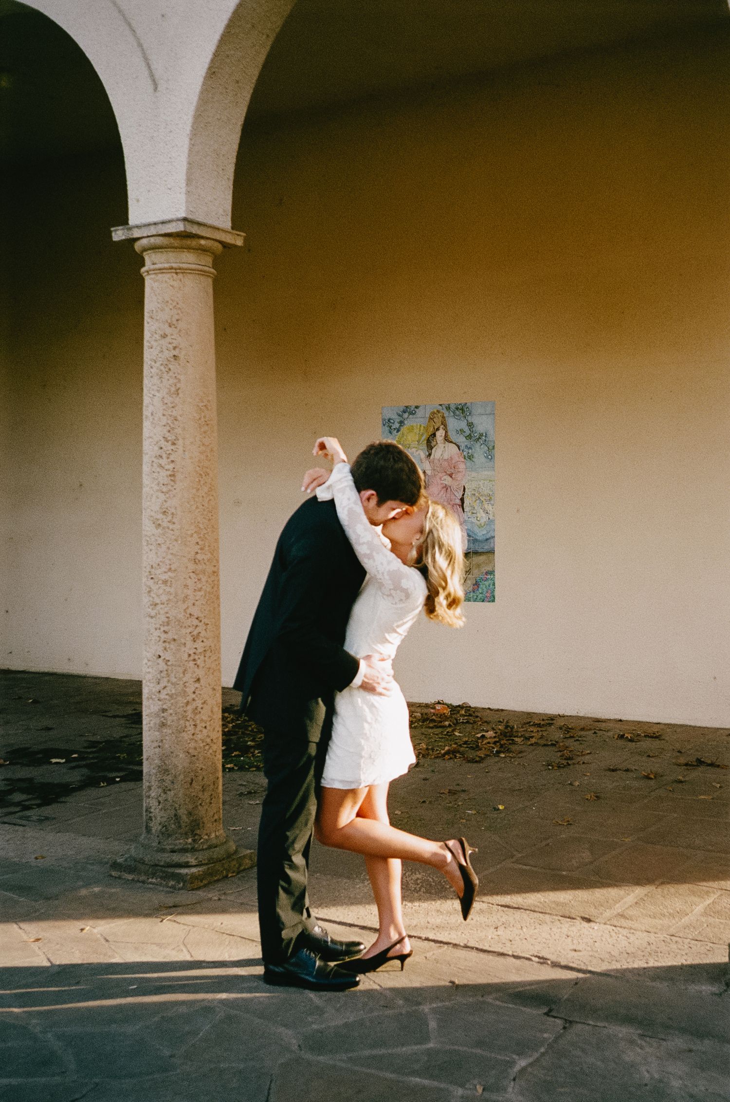 A romantic dip pose between a couple in formal attire under stone archways.