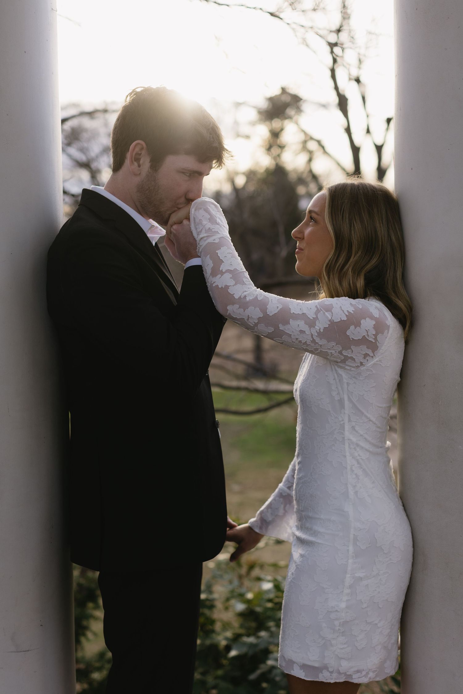 A couple embraces between white columns during a sunset engagement photoshoot.