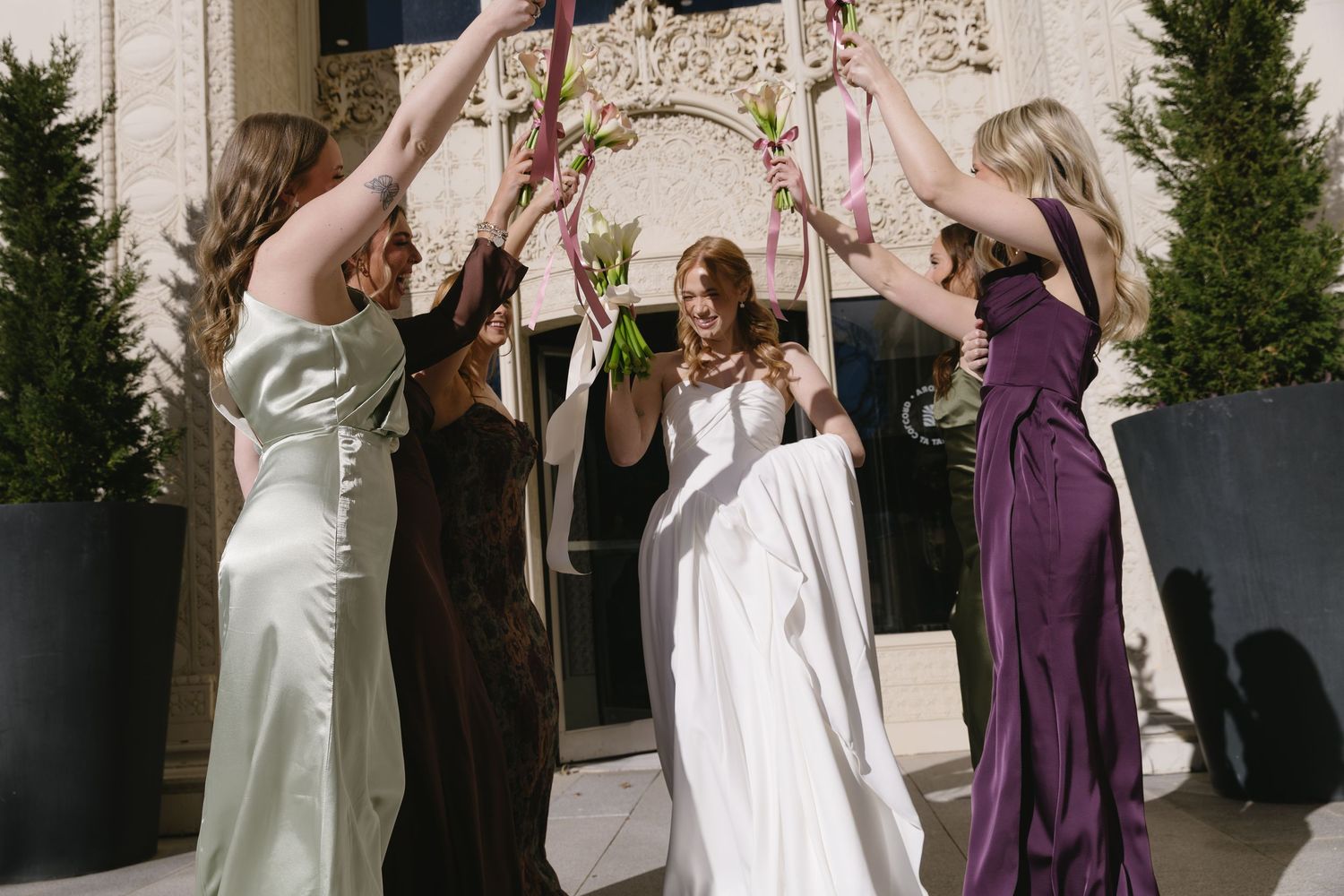 Bridal party in purple and sage green dresses gathered outdoors for candid photos.