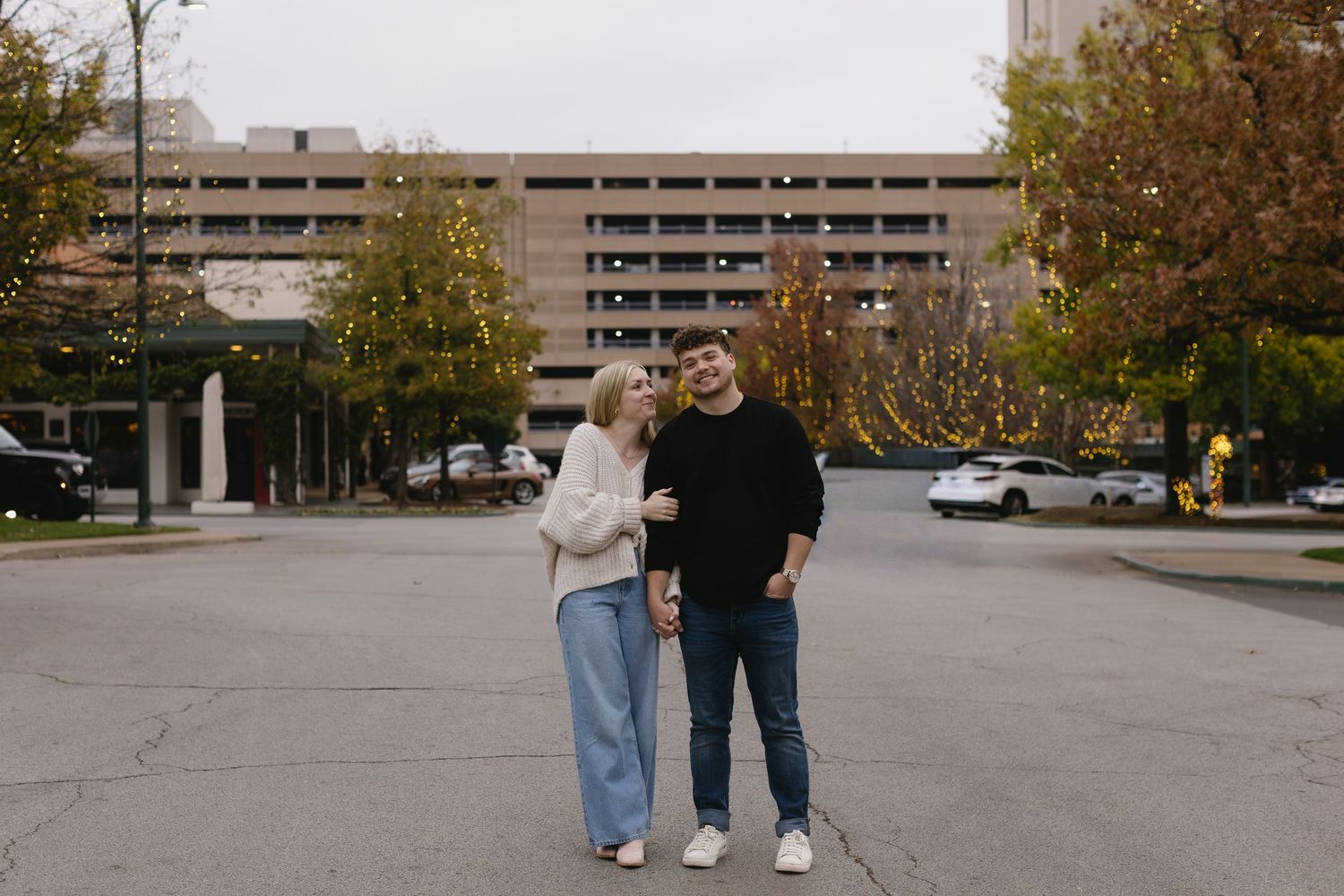 A couple walks together through an urban setting with parking structures in the background.