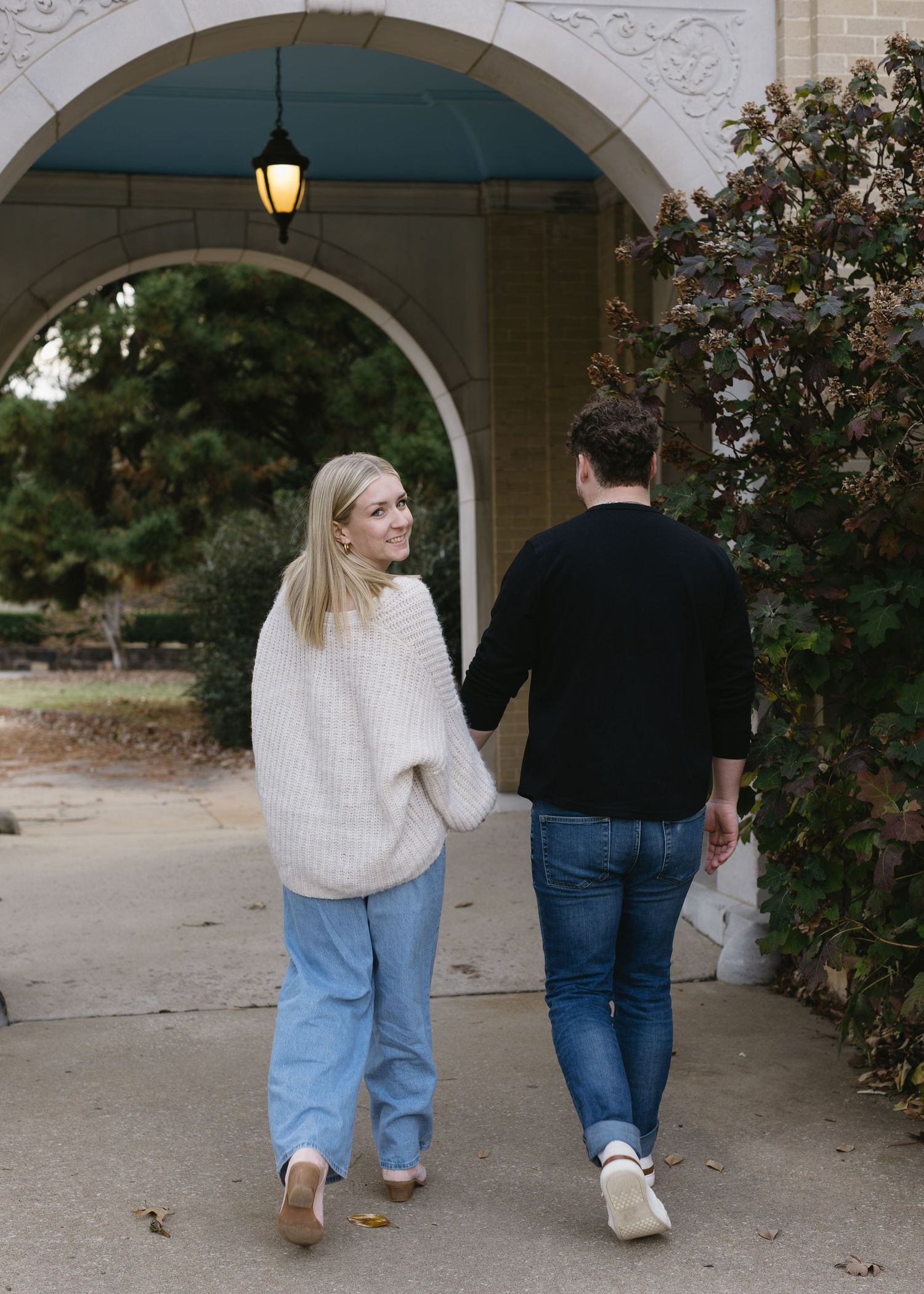A couple walking together under arched walkways wearing casual outfits of jeans and sweaters.