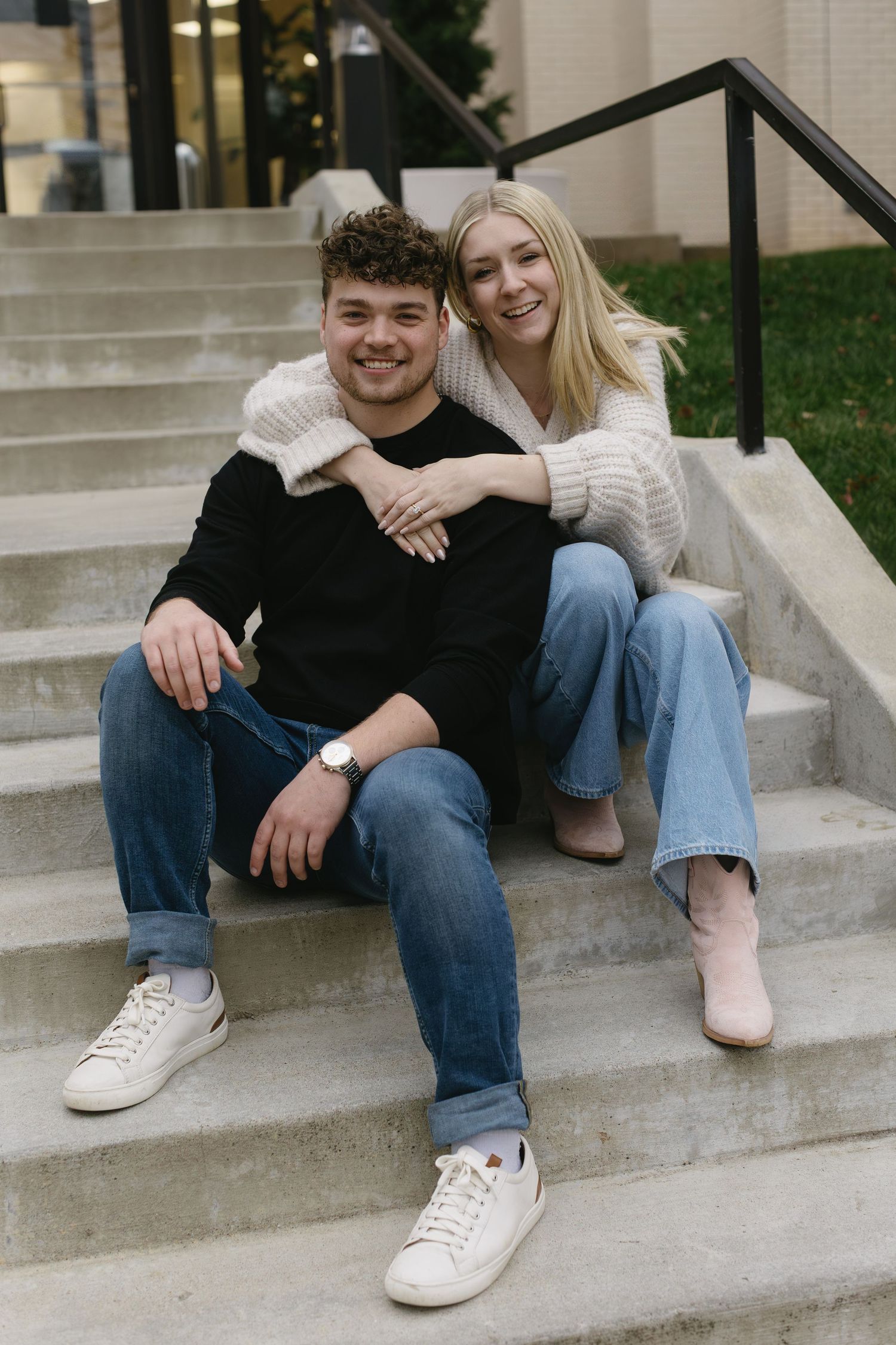 A couple in casual attire sharing tender moments while sitting on outdoor steps.