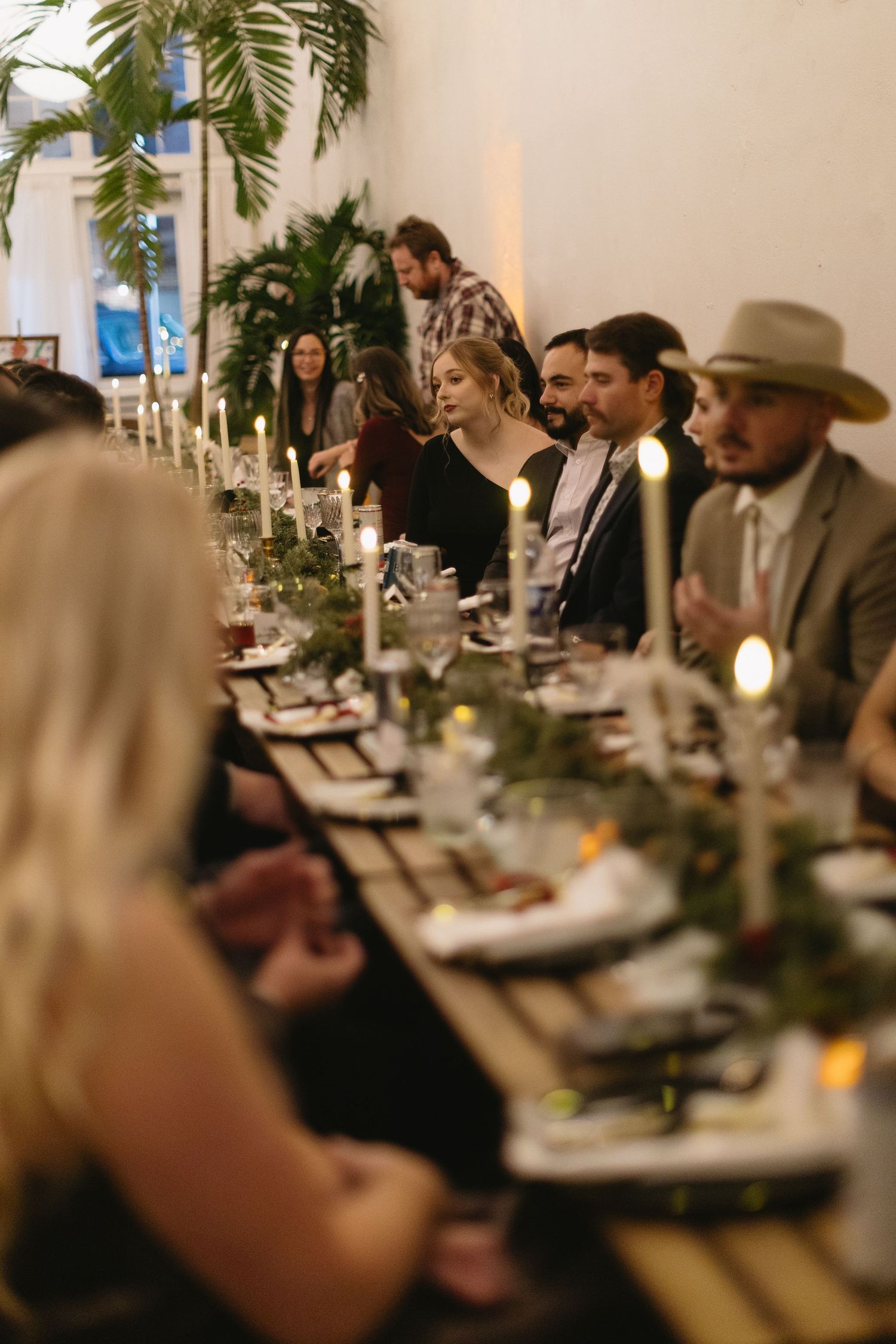 Diners seated at an elegant restaurant table with palm plants creating a tropical ambiance in soft lighting.