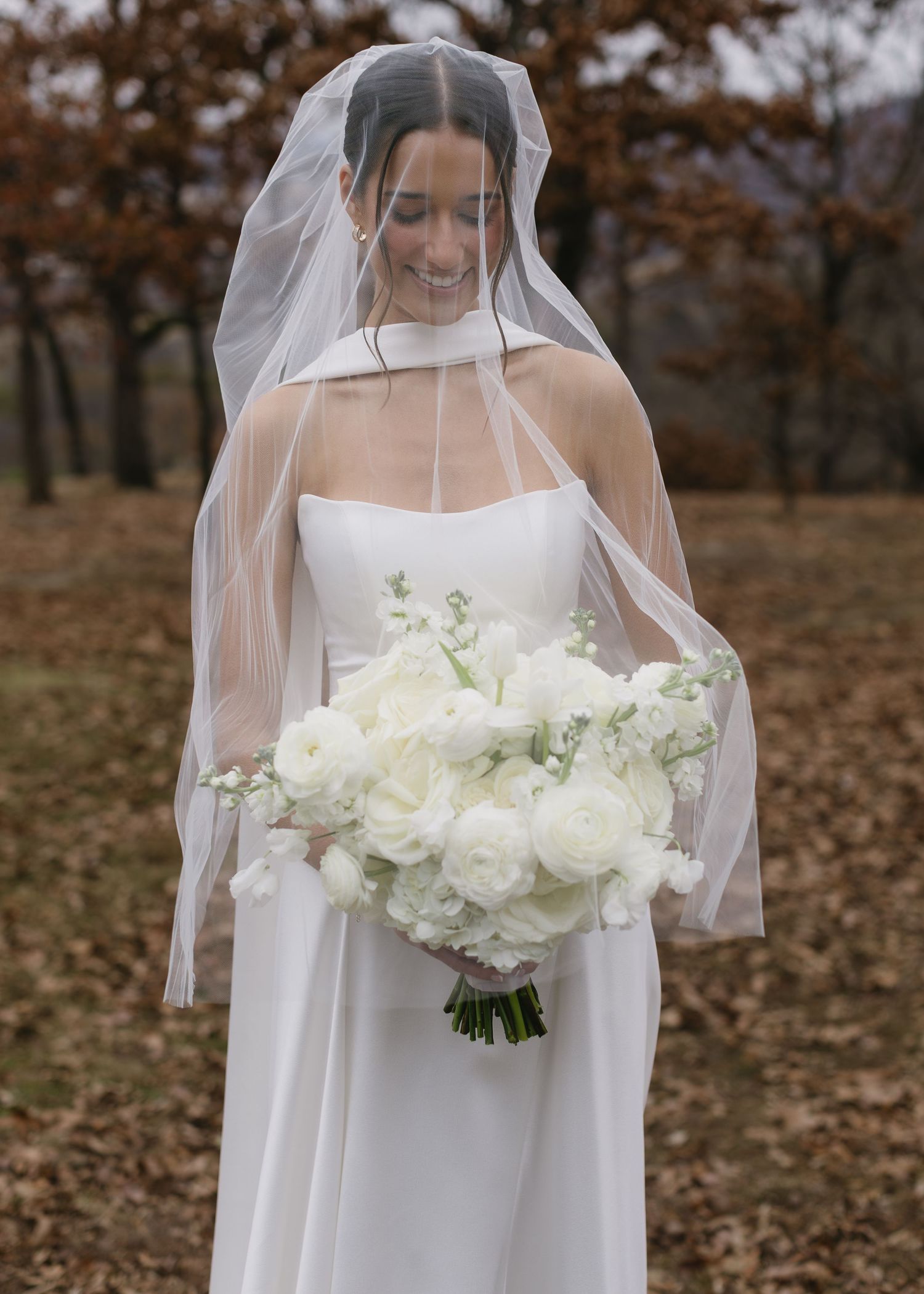 A romantic bridal portrait with flowing veil and white rose bouquet in autumn setting.