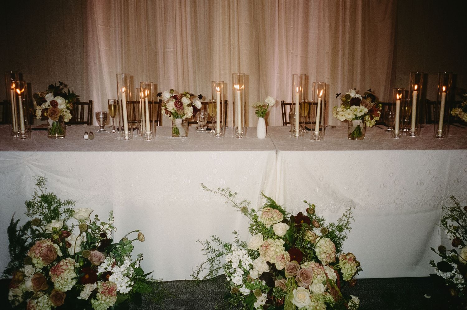 Elegant wedding reception decor with white floral centerpieces and candles along tables.