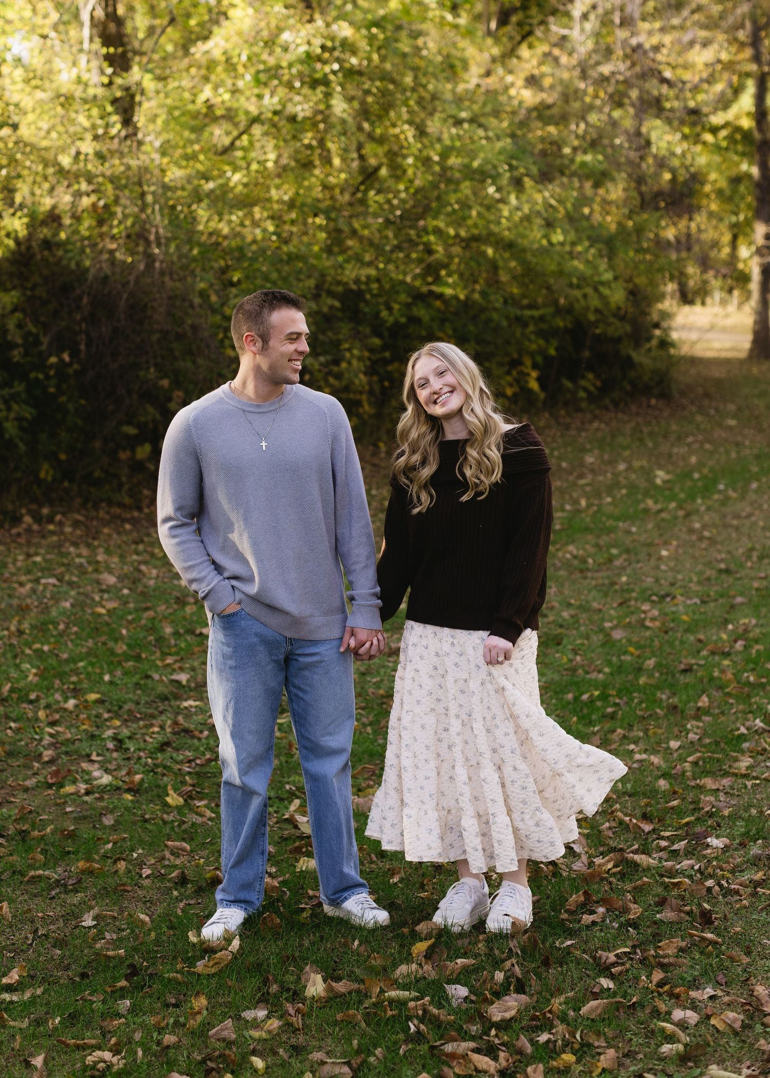 A couple playfully poses together in a park filled with autumn leaves.