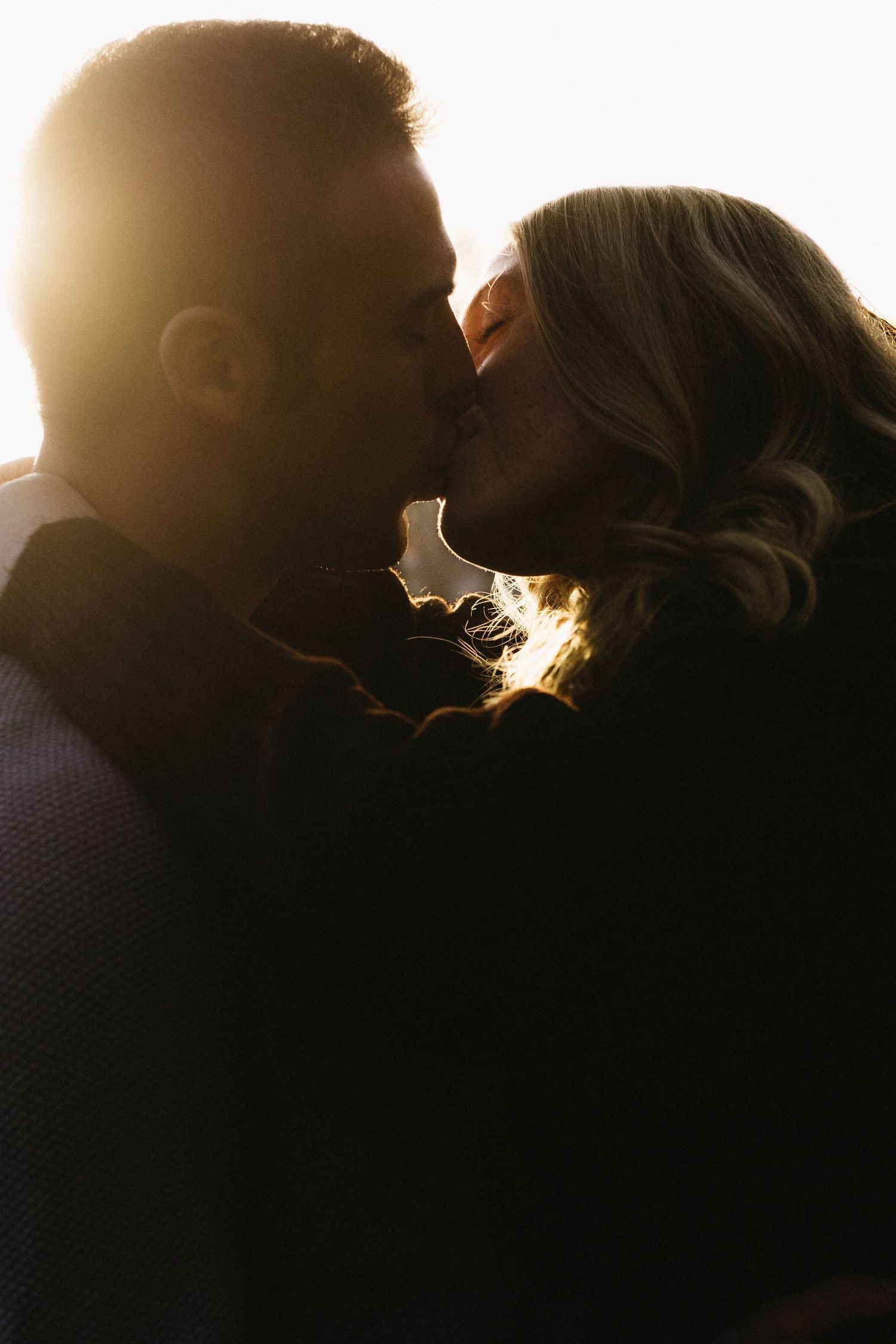 Silhouetted couple sharing an intimate kiss in golden sunlight creating a romantic backlit glow.