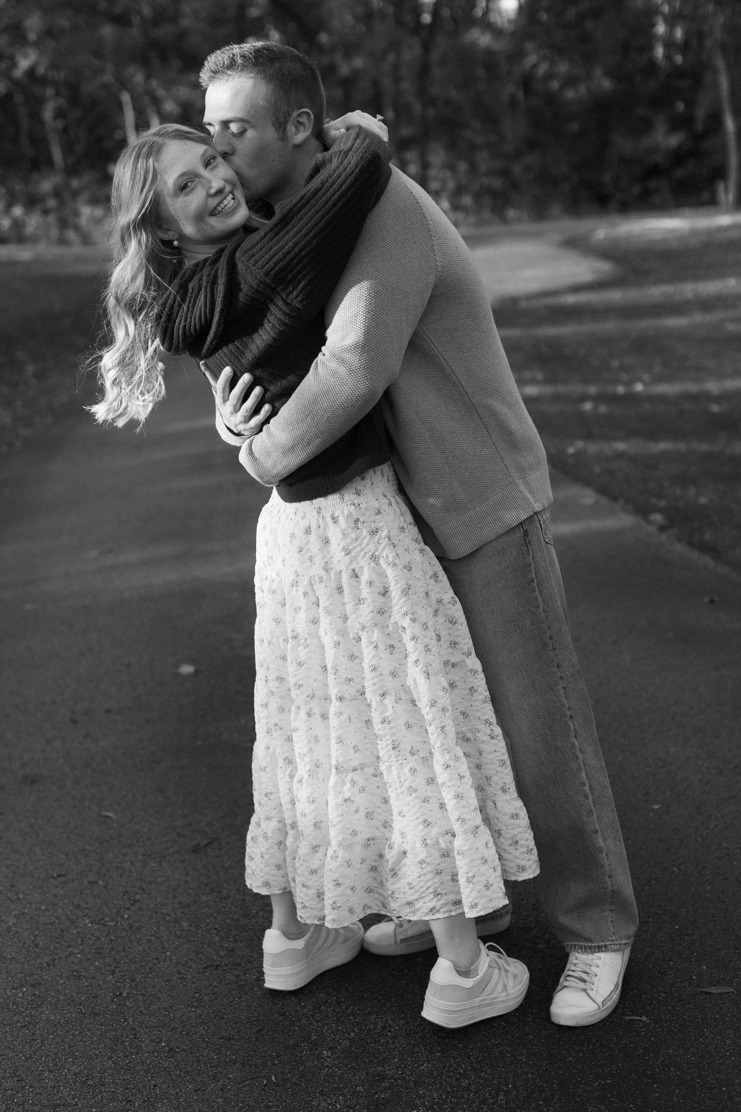 Black and white photo of couple embracing on path with romantic lighting.