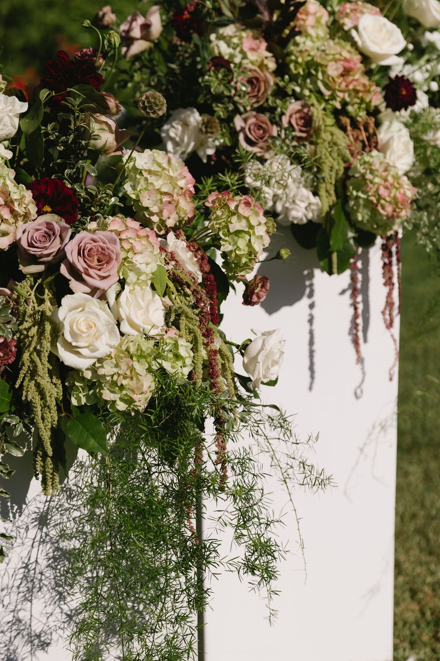 Lush floral arrangement with pink roses and cascading greenery decorates a white wedding backdrop.