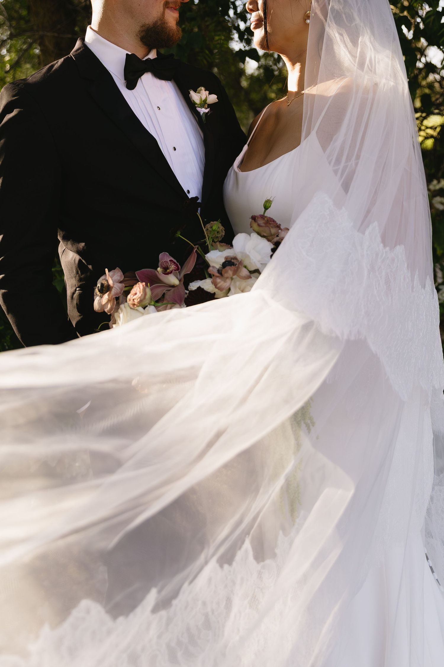 Bride's white veil flows dramatically in the wind during outdoor wedding portraits.