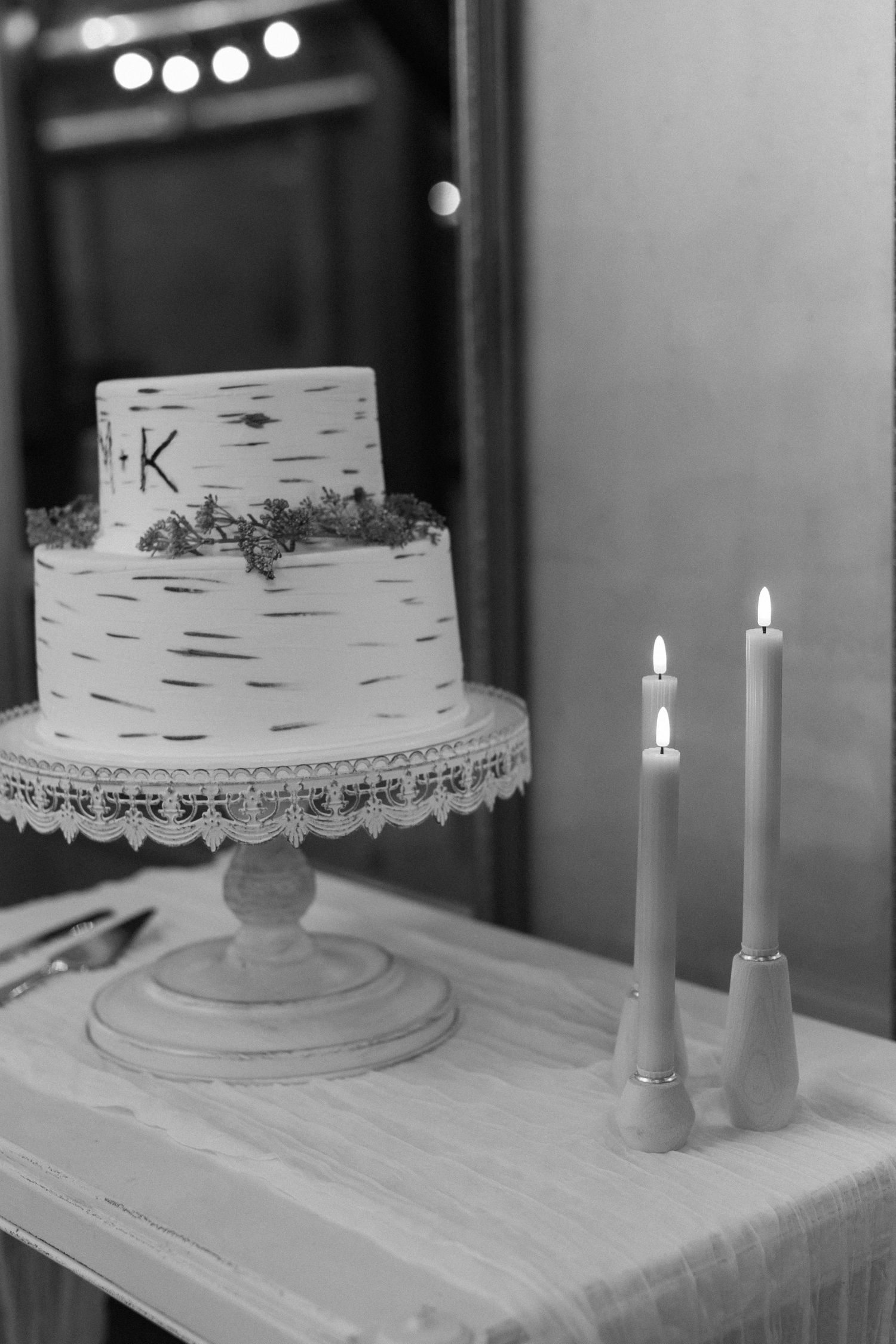 White wedding cake with birch bark texture and lit candles on display at reception.