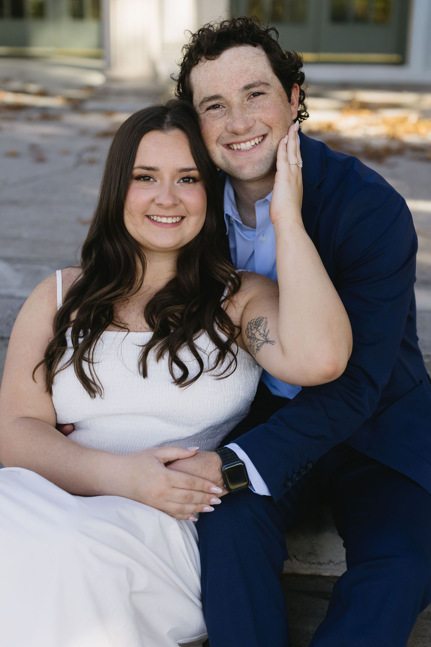 A couple poses together outdoors wearing white and navy blue outfits during a photo session.