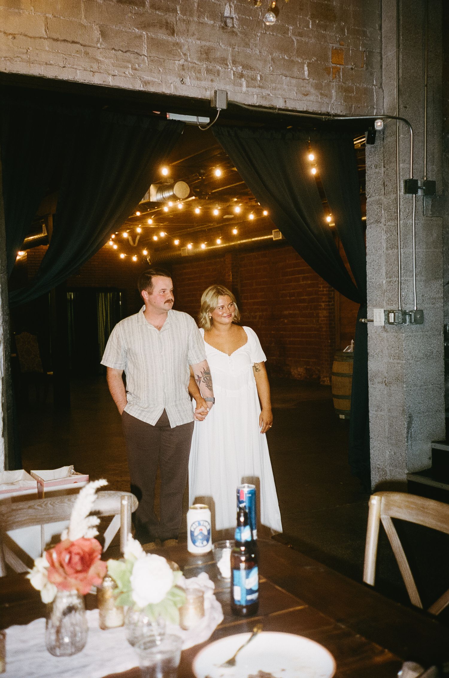 Wedding couple standing in doorway with string lights and table settings in foreground.