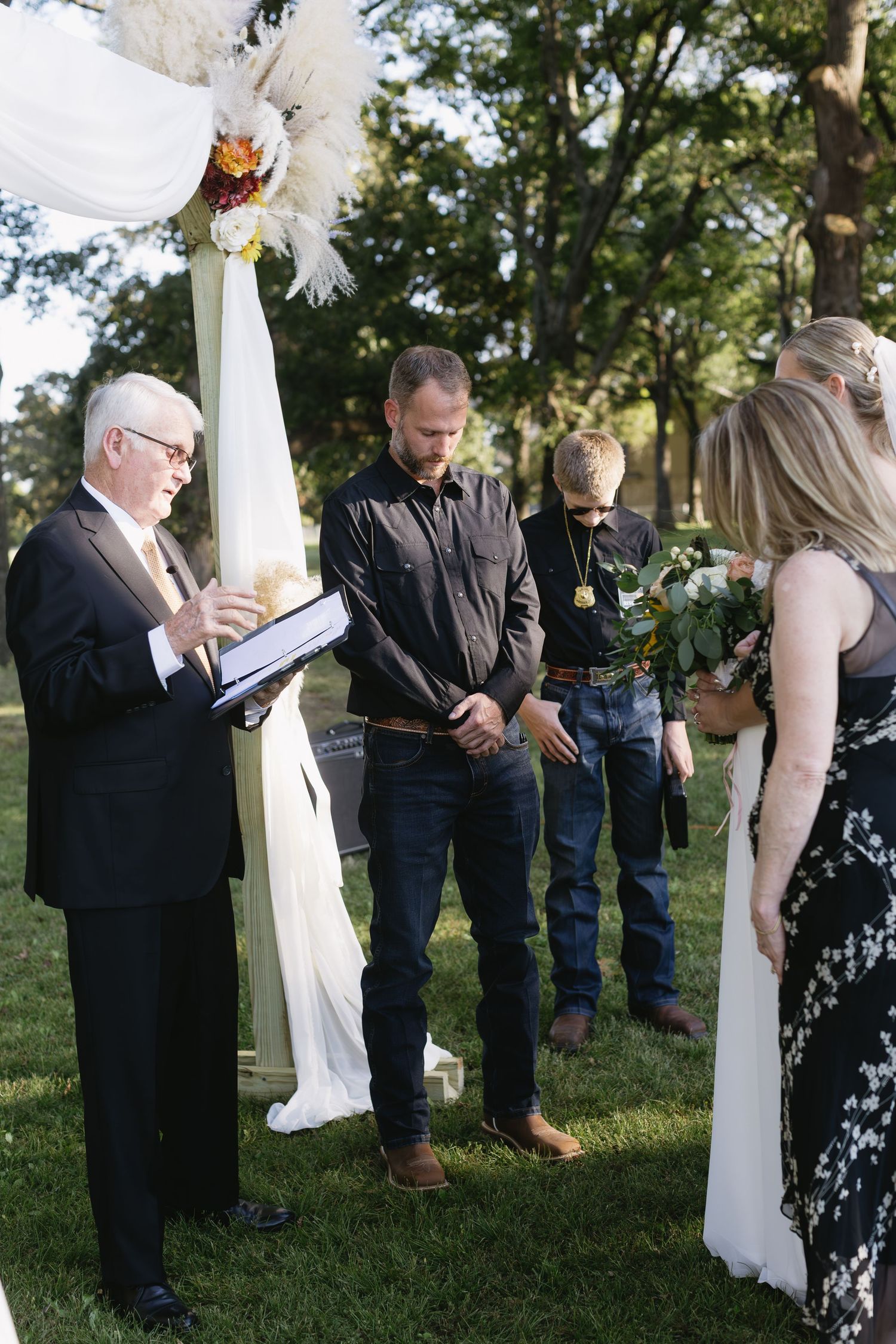 An outdoor wedding ceremony with white fabric draped posts and an officiant reading from a book.