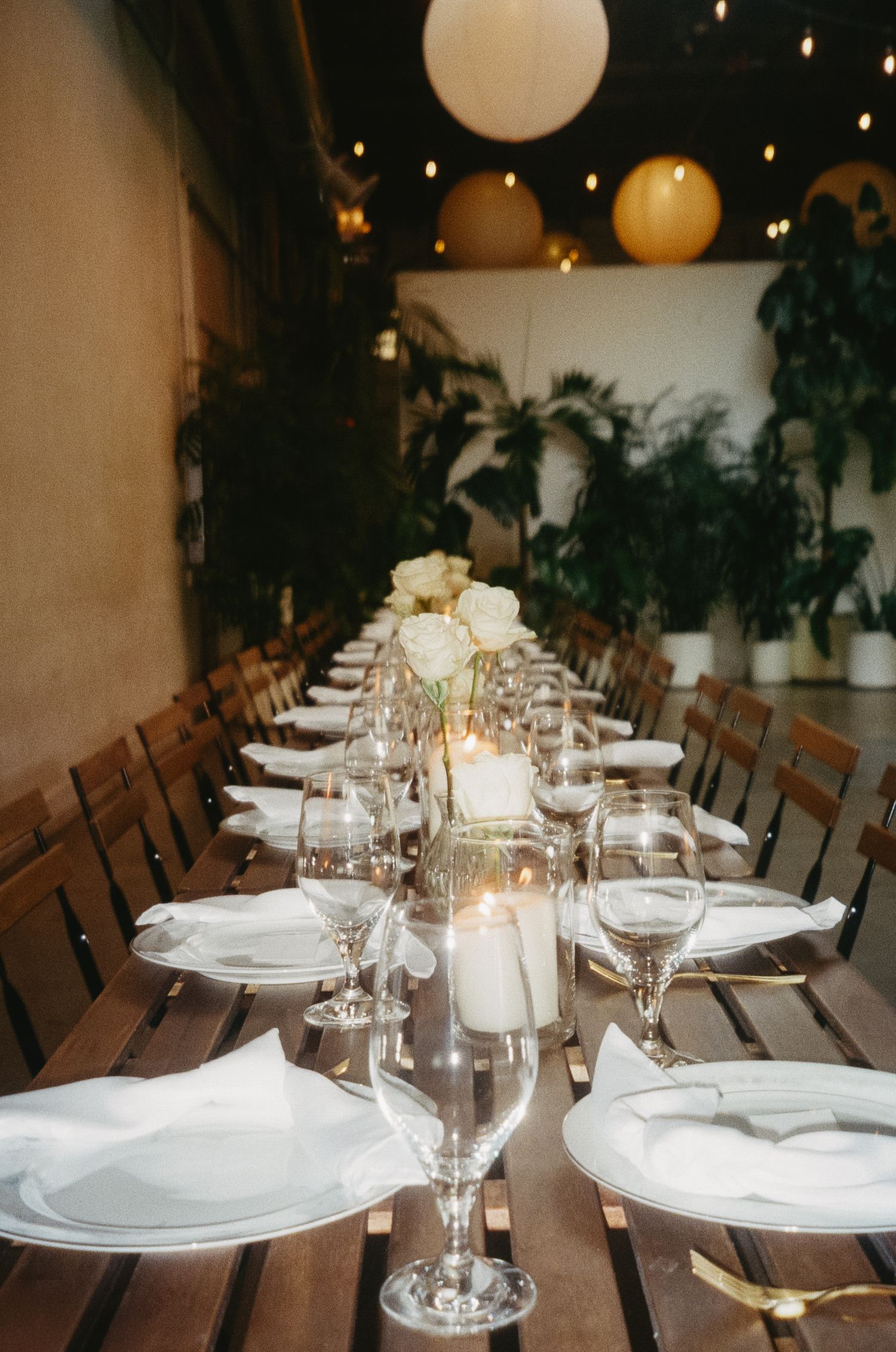 Elegant dining table setup with white plates, wine glasses and paper lanterns creating a romantic ambiance.