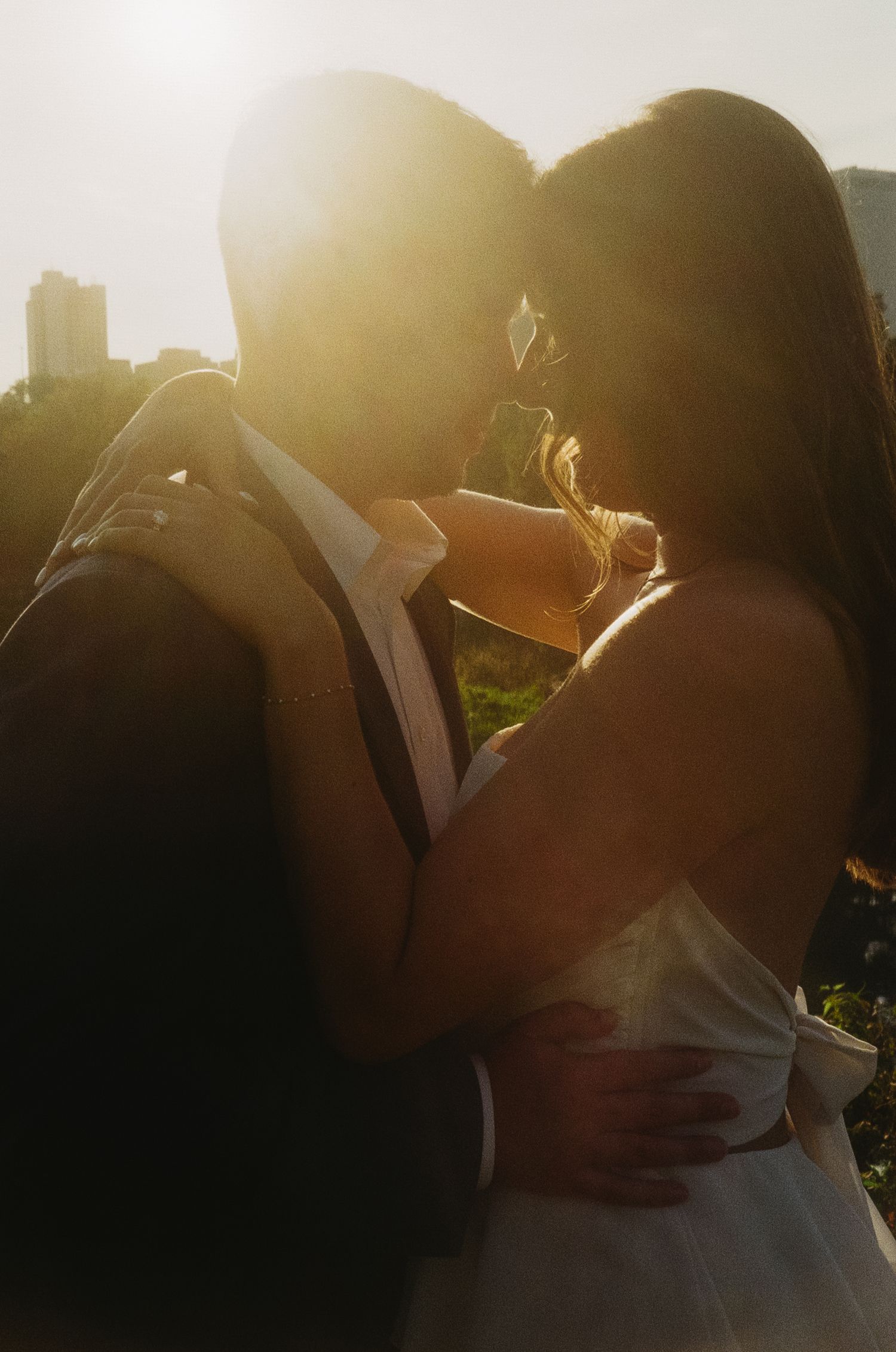 A romantic silhouetted couple embraces during golden hour with sun flare creating a dreamy backlit effect.
