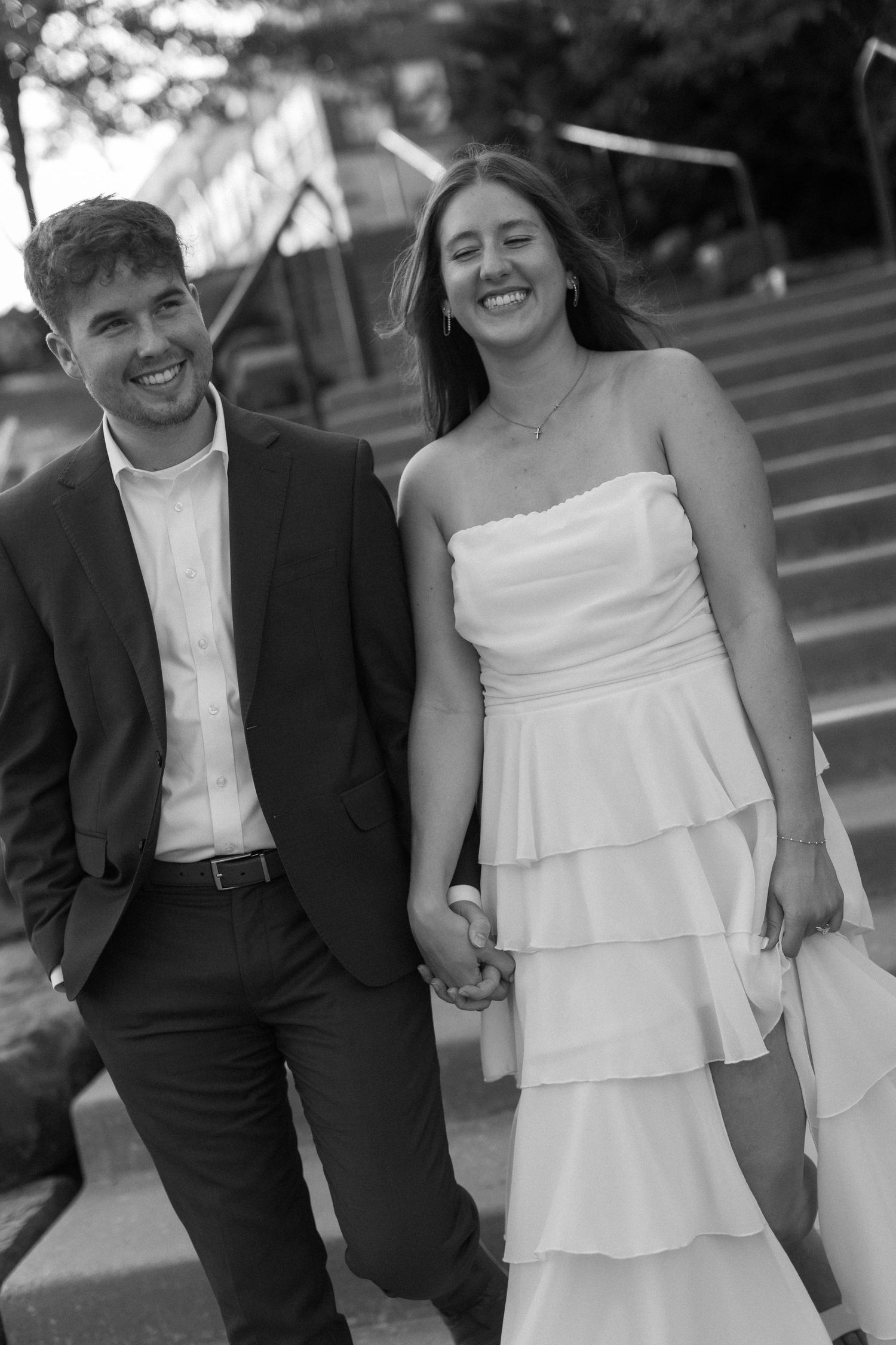 A couple walks together laughing in formal attire on a sunny day.