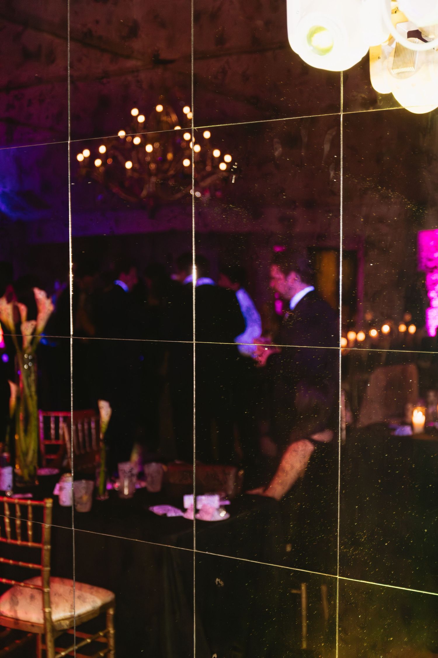 Dark reception venue with string lights and silhouettes of guests dancing in the background.