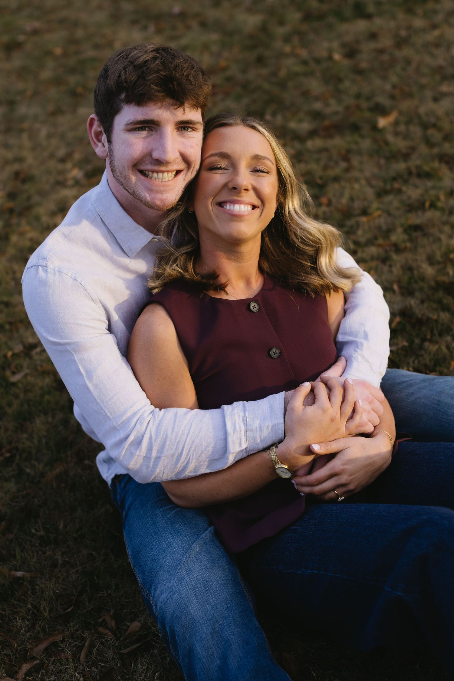 Happy couple sharing a joyful embrace while sitting on grass outdoors.