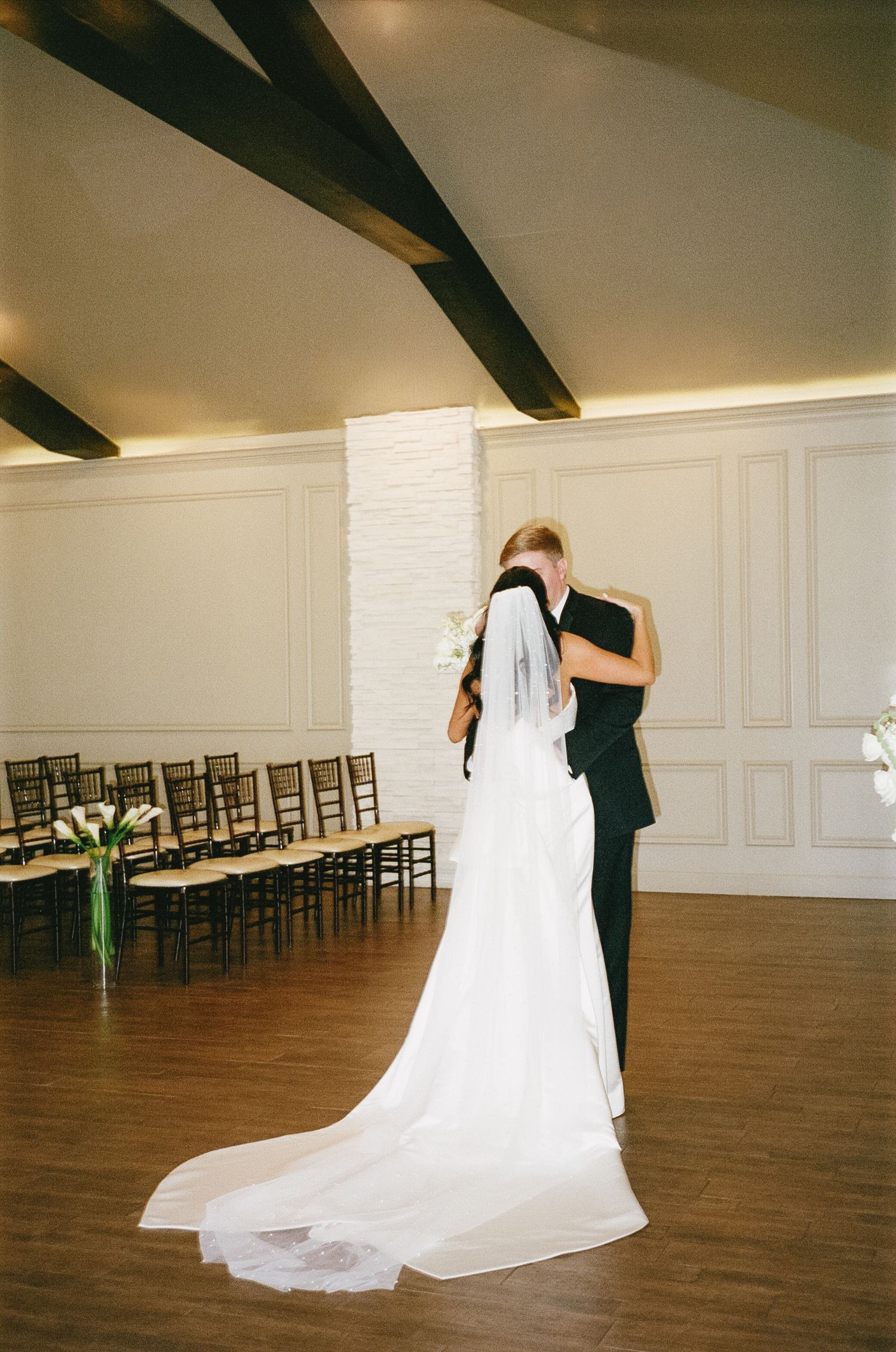 A wedding couple's first dance sequence captured in a spacious ballroom with wooden floors and white walls.