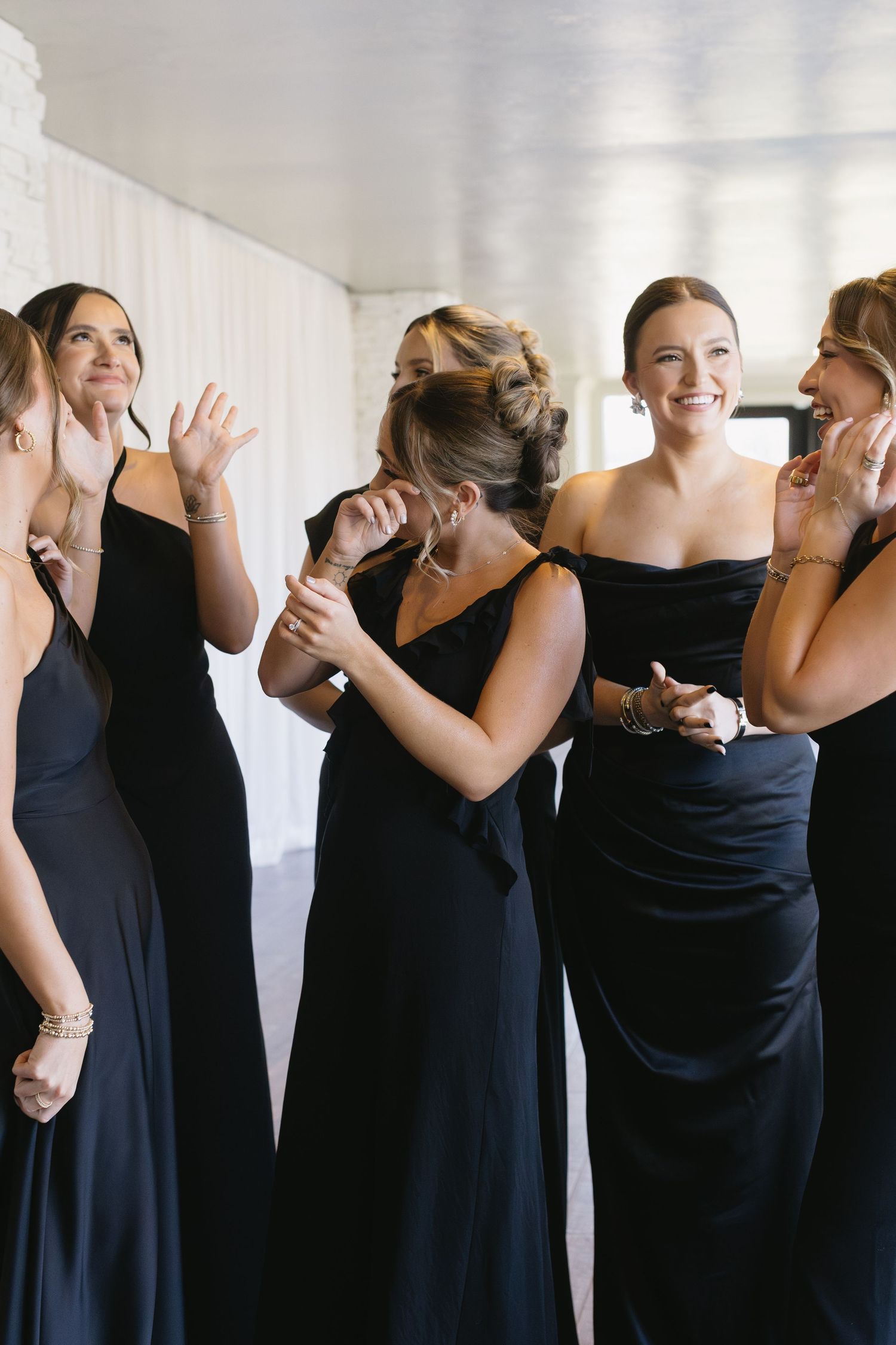 Bridesmaids wearing matching black dresses share excited reactions during wedding preparations.